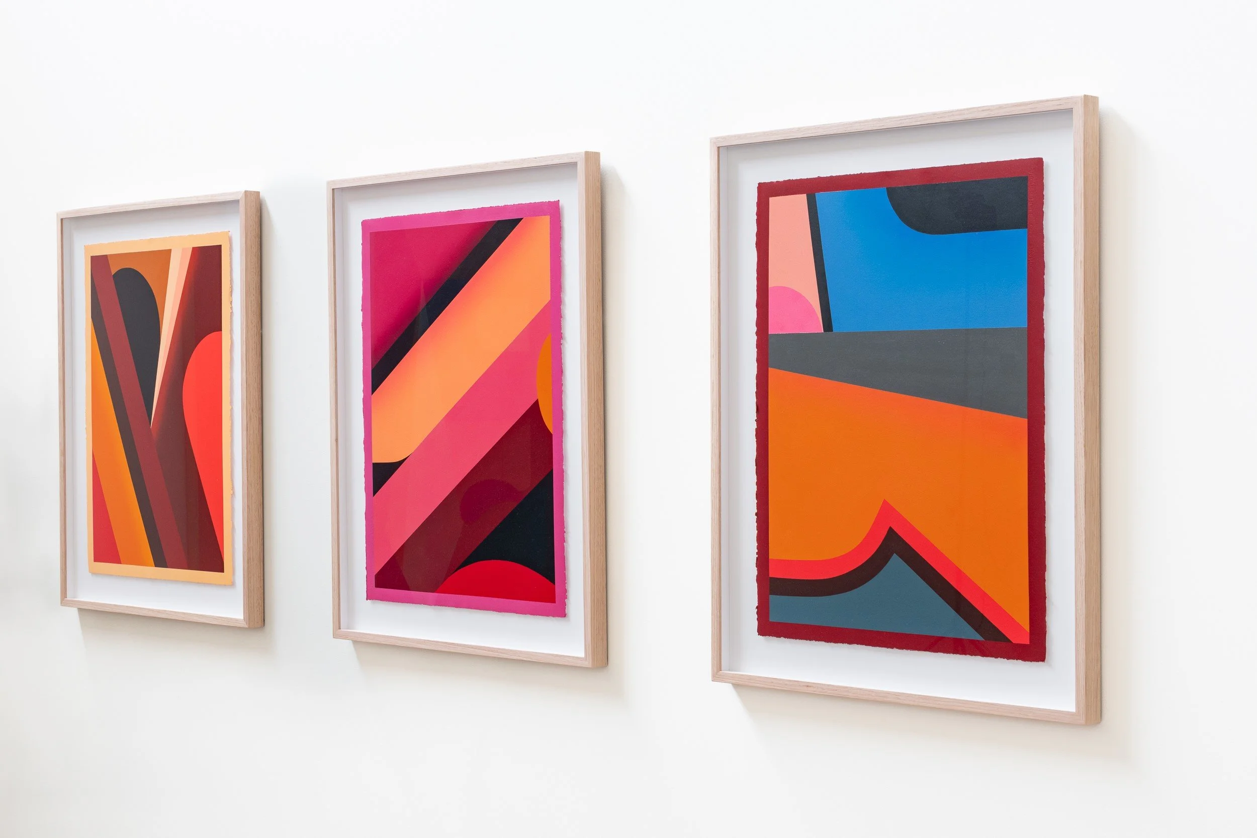 Three abstract colorful geometric paintings hanging on a white wall in a gallery.