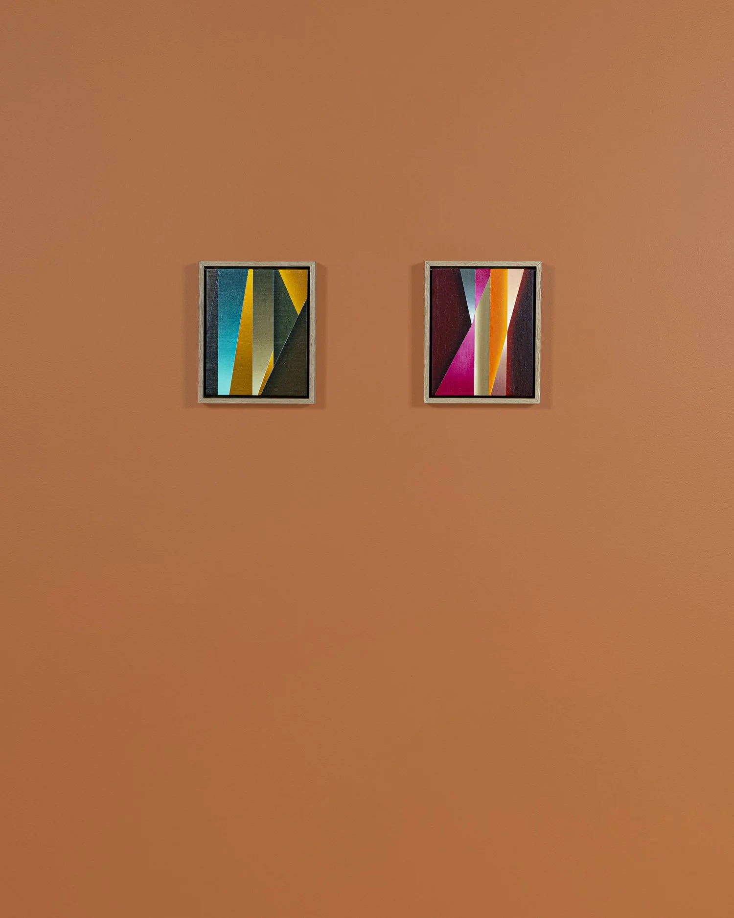 Two framed geometric abstract art pieces hung on an orange wall.