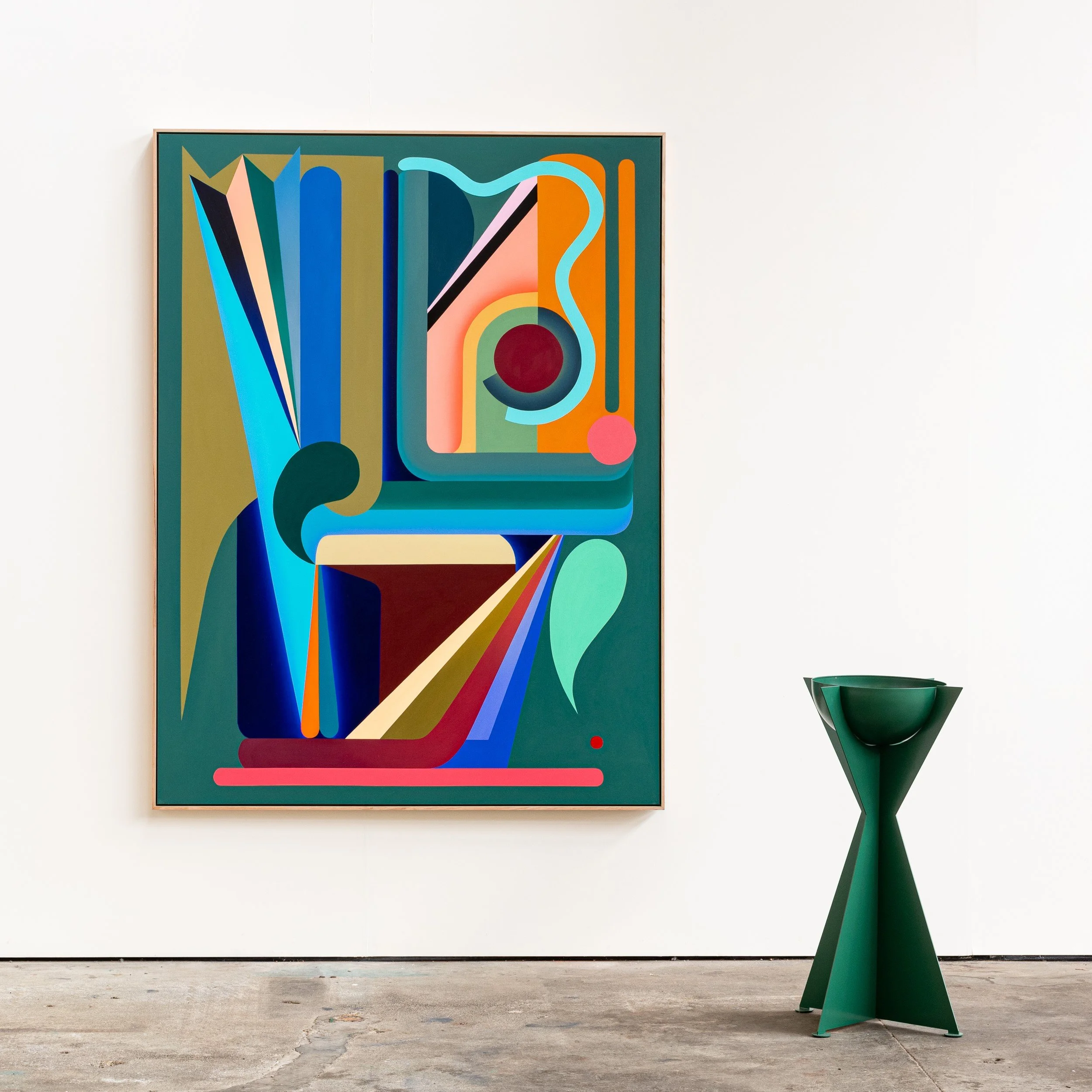 Abstract colorful geometric artwork hanging on a white wall in an art gallery, with a green modern sculpture in front.