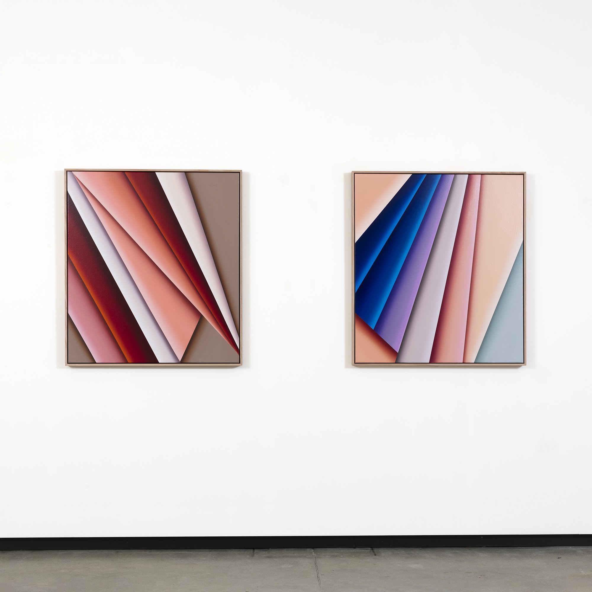 Two framed abstract art pieces with colorful diagonal shapes hanging on a white gallery wall.