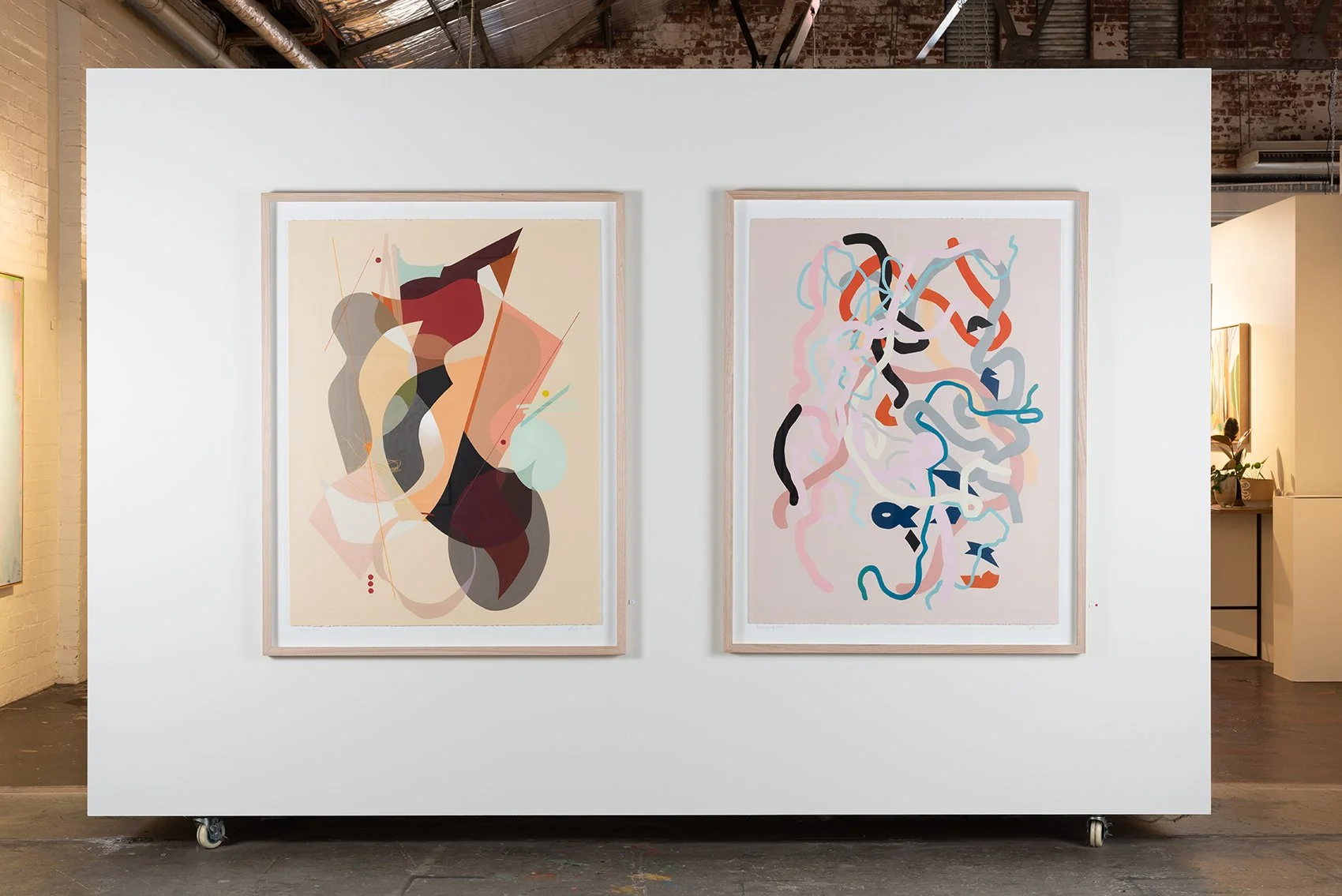 Two abstract art paintings hanging on a white wall in an art gallery.