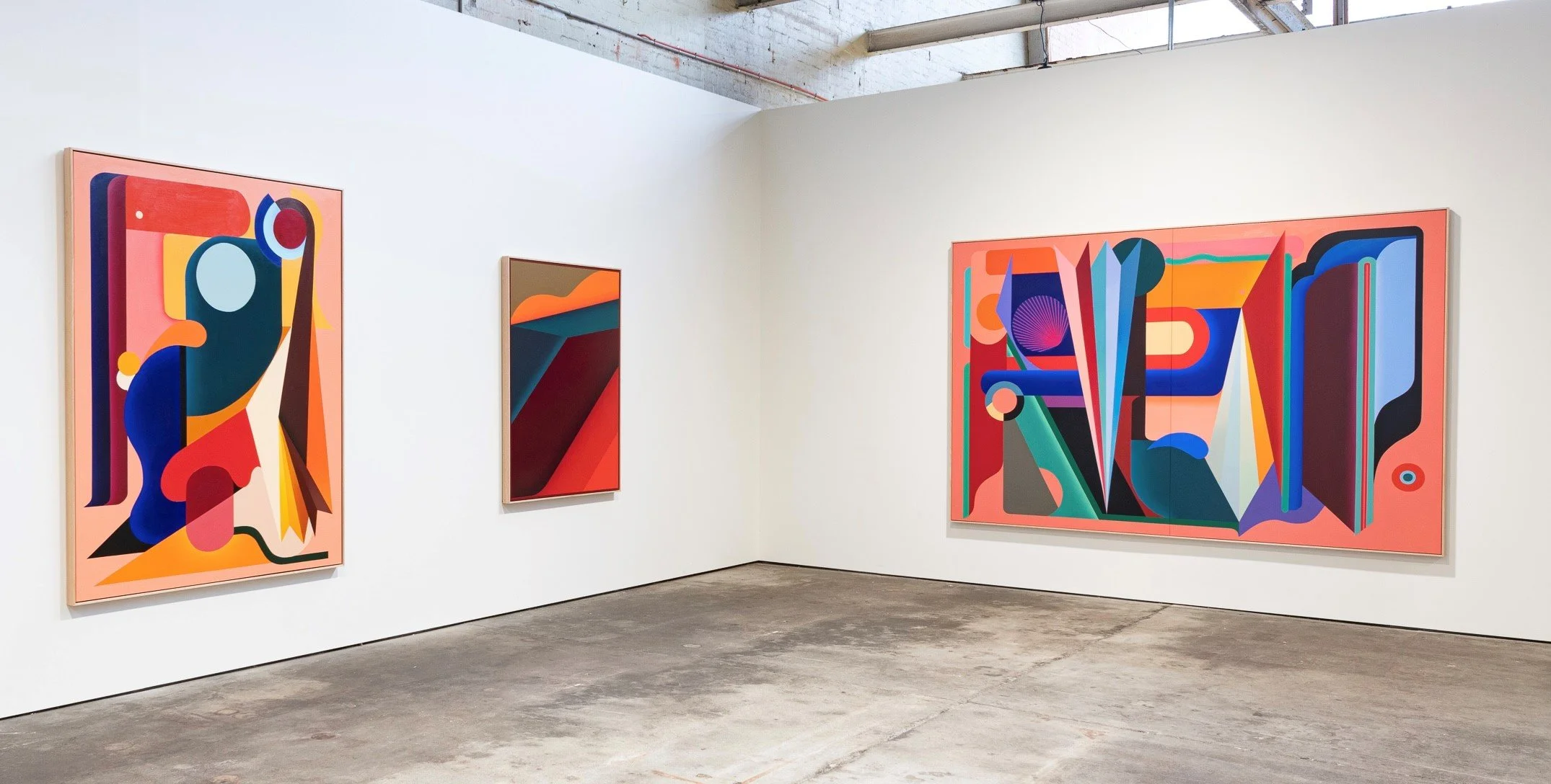 Abstract colorful geometric paintings displayed in a modern gallery with white walls and concrete floor.