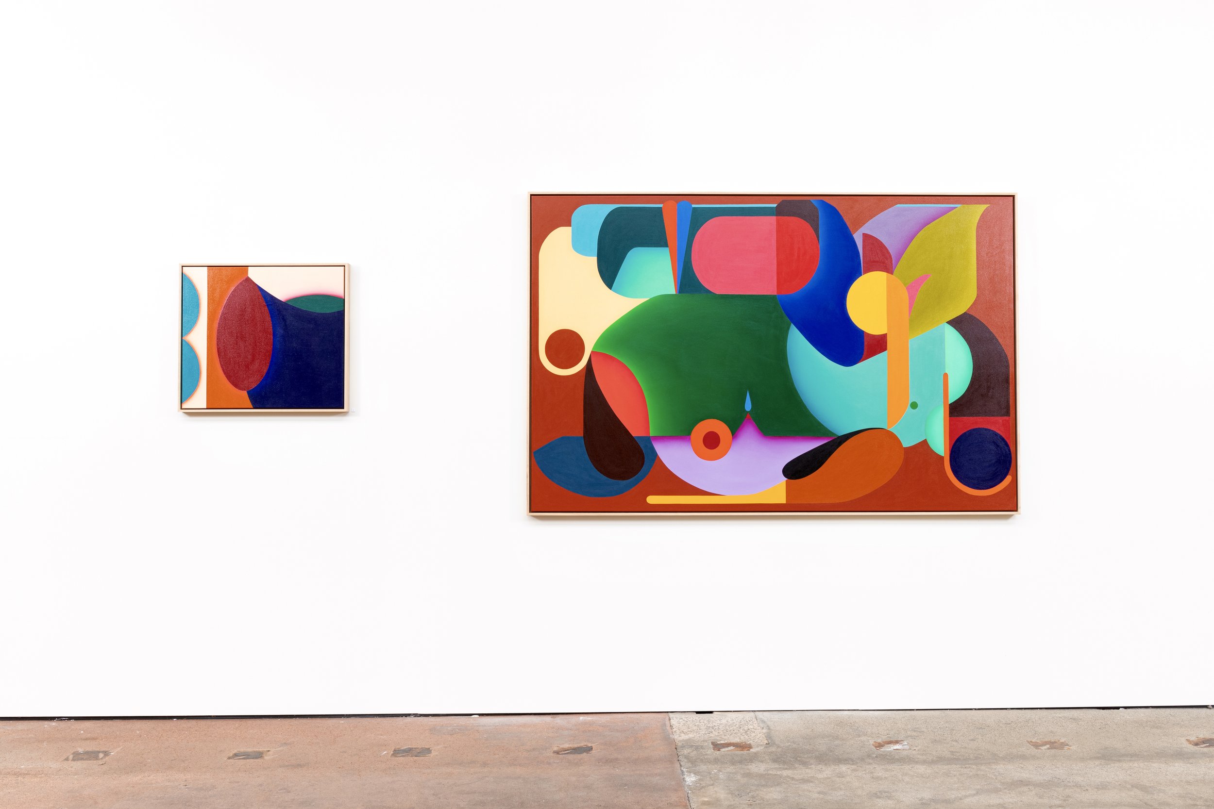 Two abstract colorful paintings on a white gallery wall, one smaller on the left, one large on the right, featuring geometric shapes and bold colors.