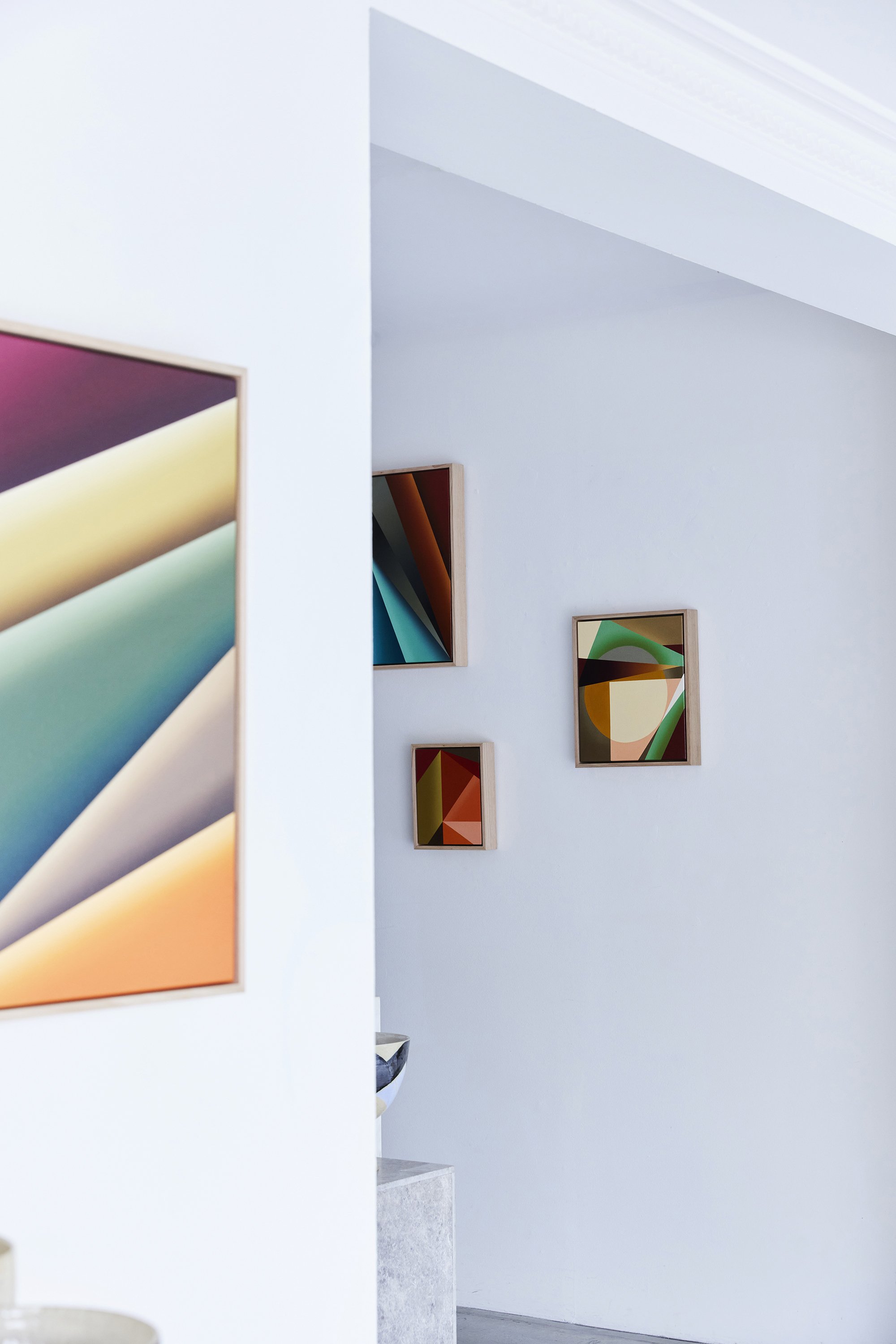 Part of an art gallery wall with colorful abstract paintings displayed on white walls.