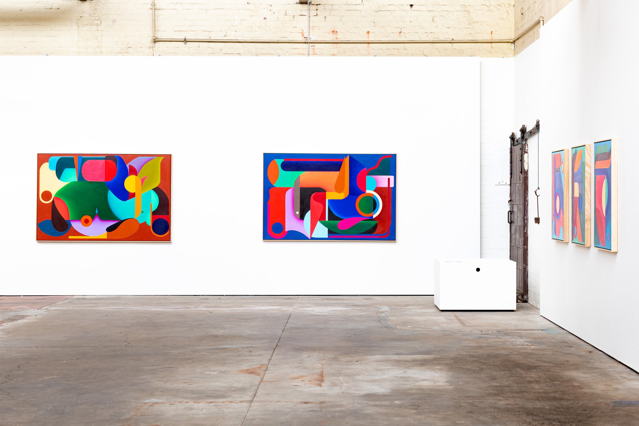 Art gallery with abstract colorful paintings on a white wall, industrial-style interior, concrete floor.