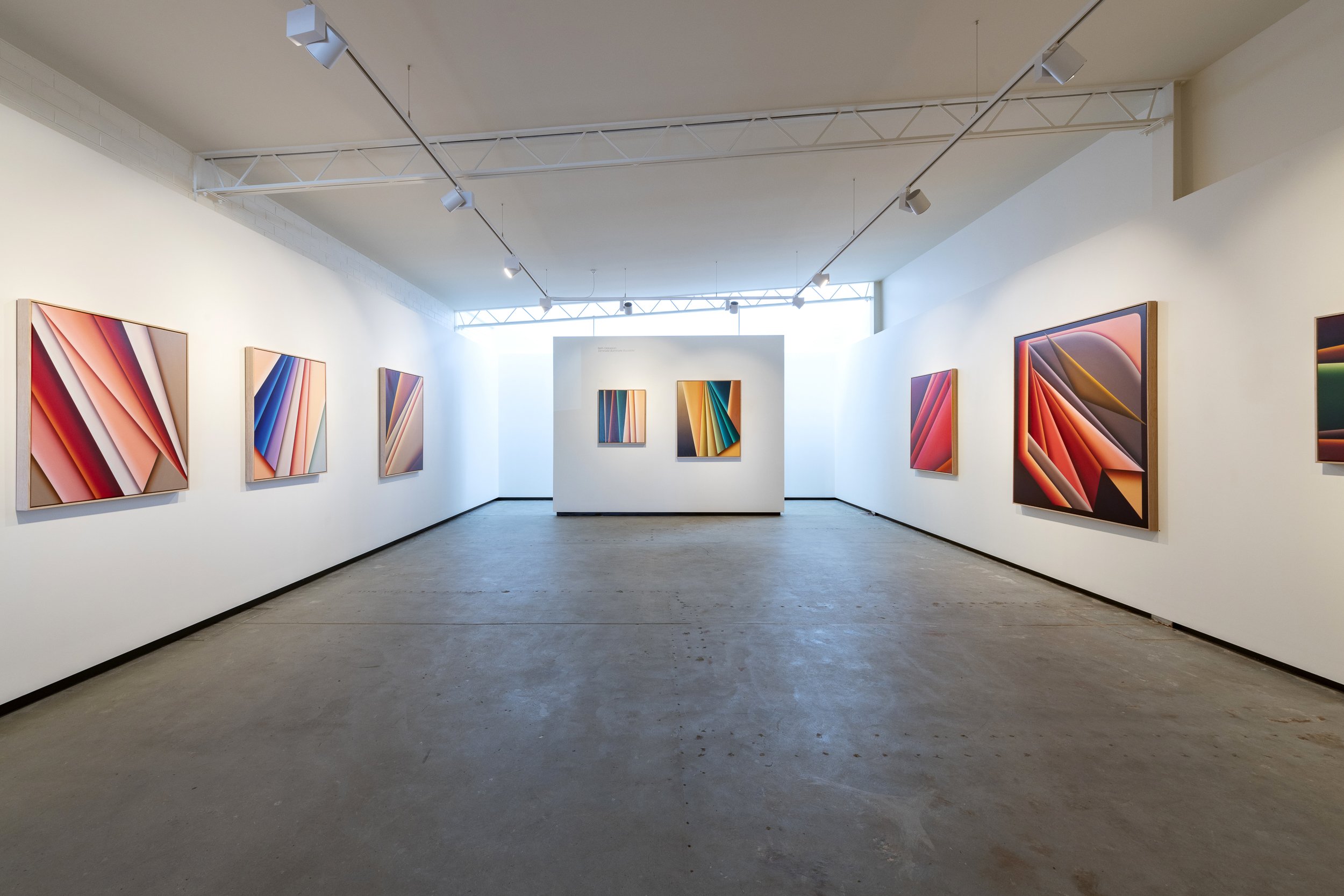 An art gallery with white walls displaying colorful abstract paintings. The artworks feature geometric shapes and bold colors, arranged in a symmetrical manner.