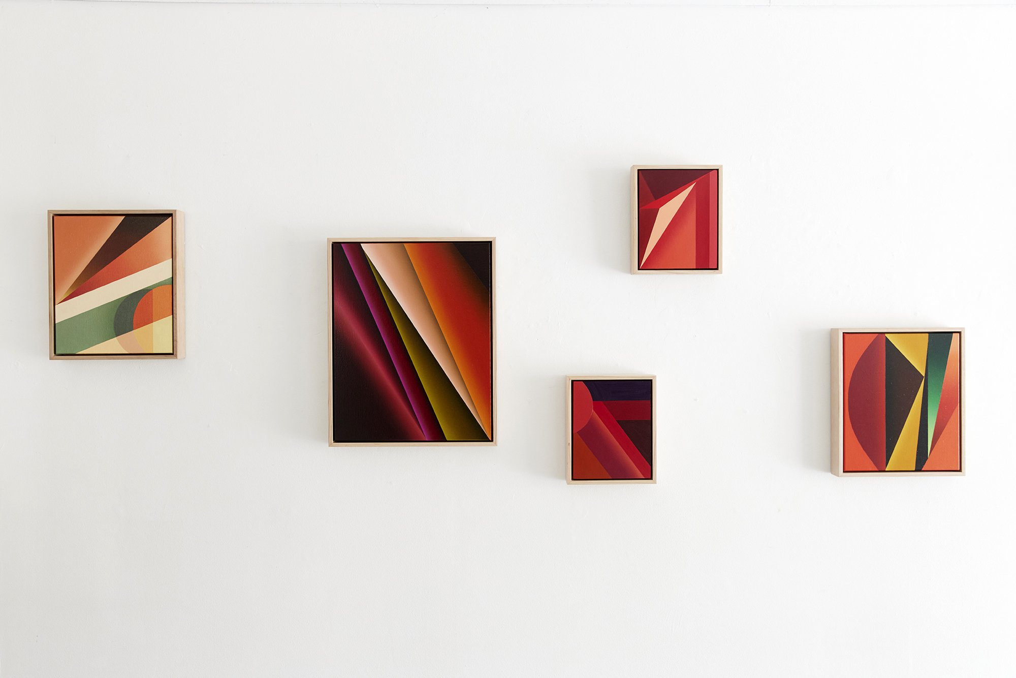Five abstract colorful paintings with geometrical shapes on a white gallery wall
