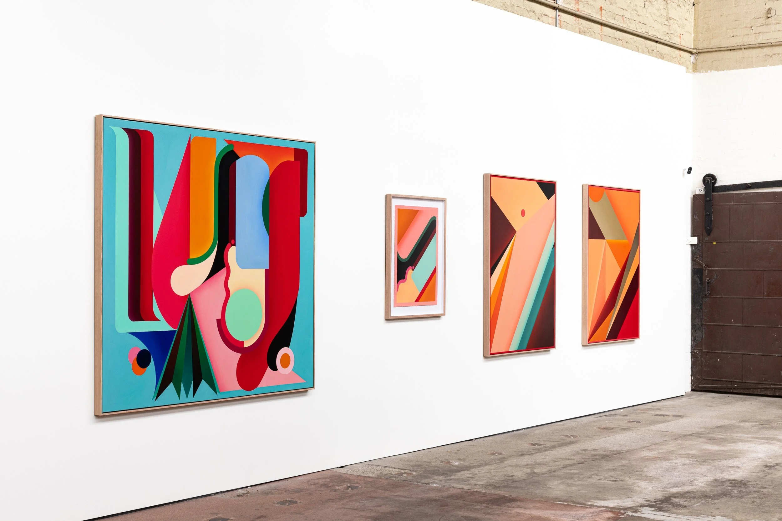 Art gallery wall showcasing four abstract colorful paintings with geometric designs.