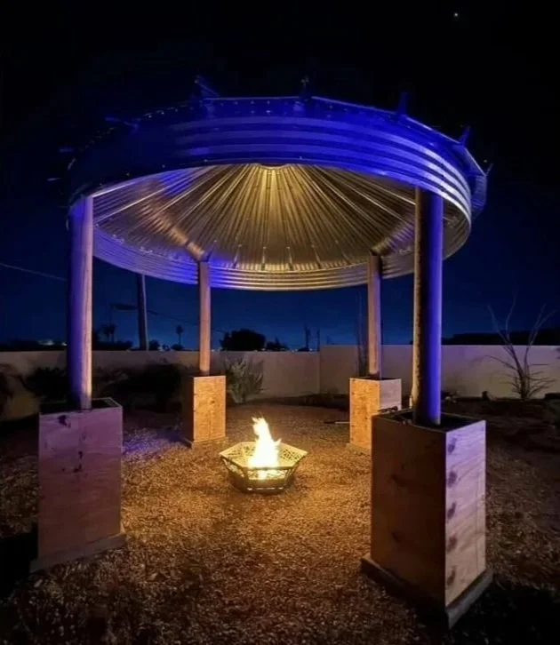 Outdoor fire pit with a small blaze under a modern metal and wood pavilion at night