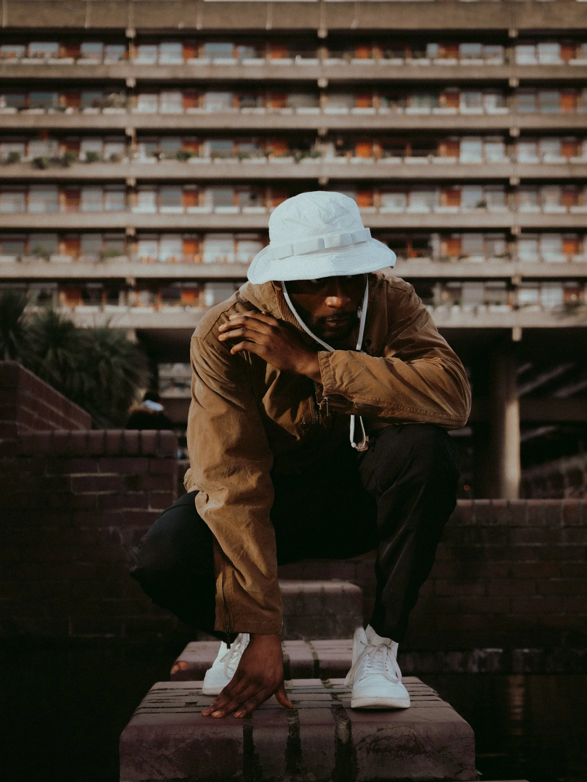 Paul Bossman crouched in a bucket hat and tan jacket in front of an estate block