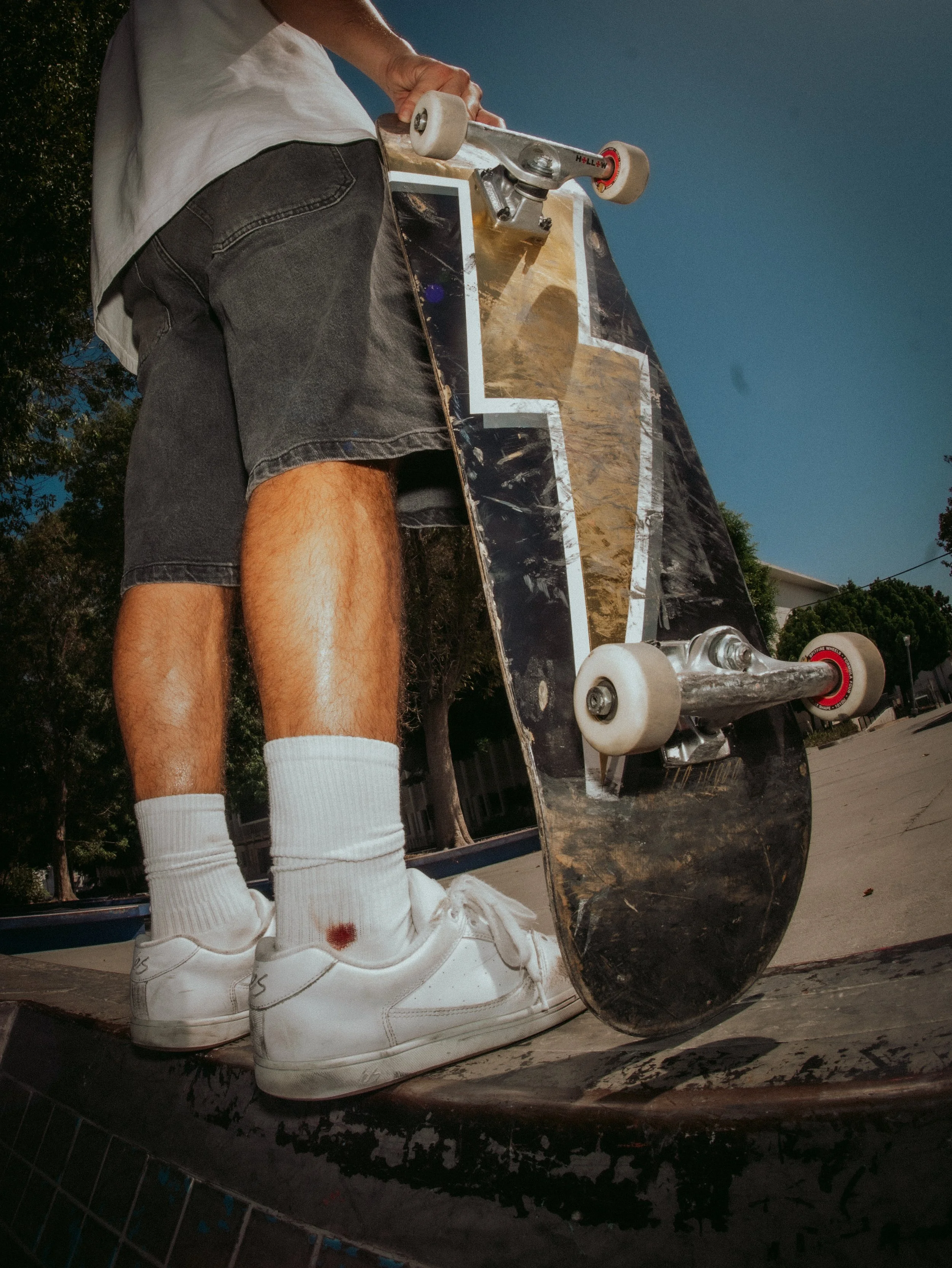Brandon Loufas holding his deck, low angle on worn sneakers at the West LA Courthouse skatepark, Los Angeles skate photography by Osy Ikhile