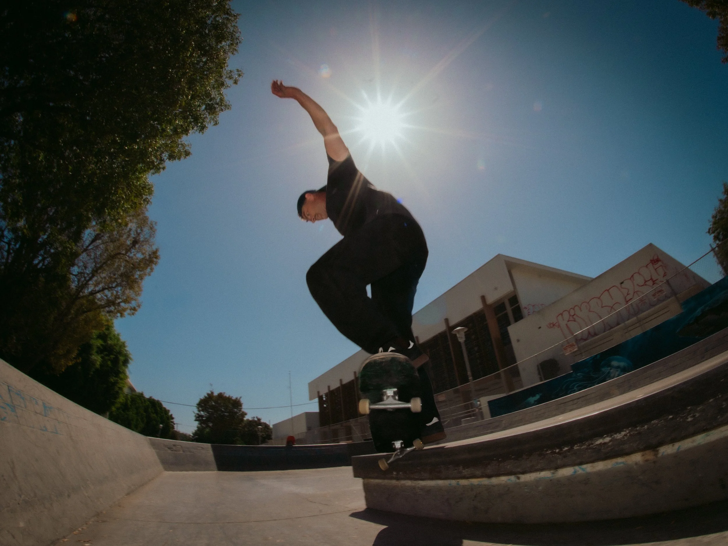 Isaiah Rojers ollies into the sun, fisheye skate shot at the West LA Courthouse skatepark, Los Angeles skate photography by Osy Ikhile