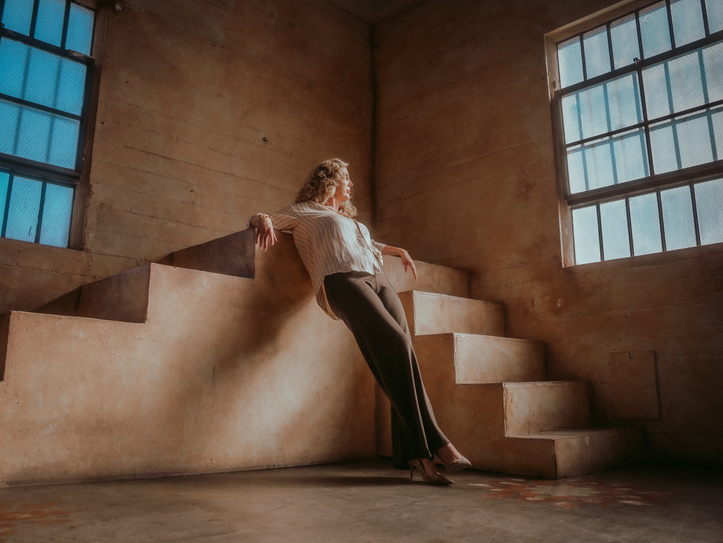 Milanka Brooks leaning on a clay staircase under tall windows, editorial fashion photography by Osy Ikhile, Los Angeles