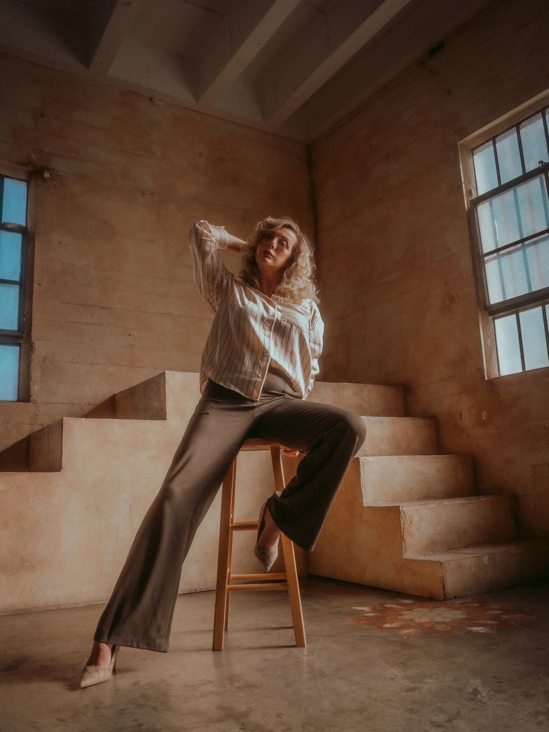 Milanka Brooks on a stool by a clay staircase and tall windows, editorial fashion photography by Osy Ikhile, Los Angeles