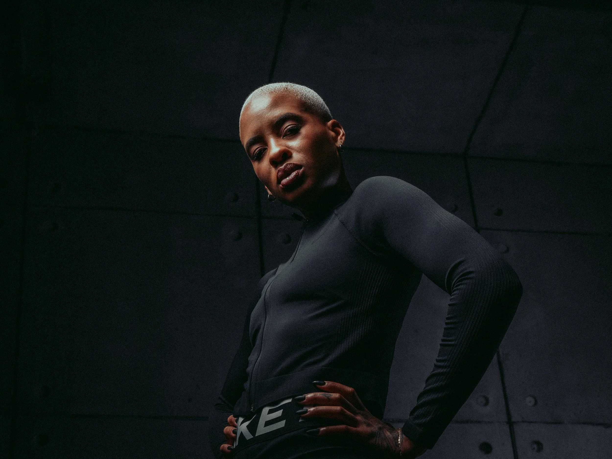 Athlete in black Nike training wear with hands on hips, low-key lighting