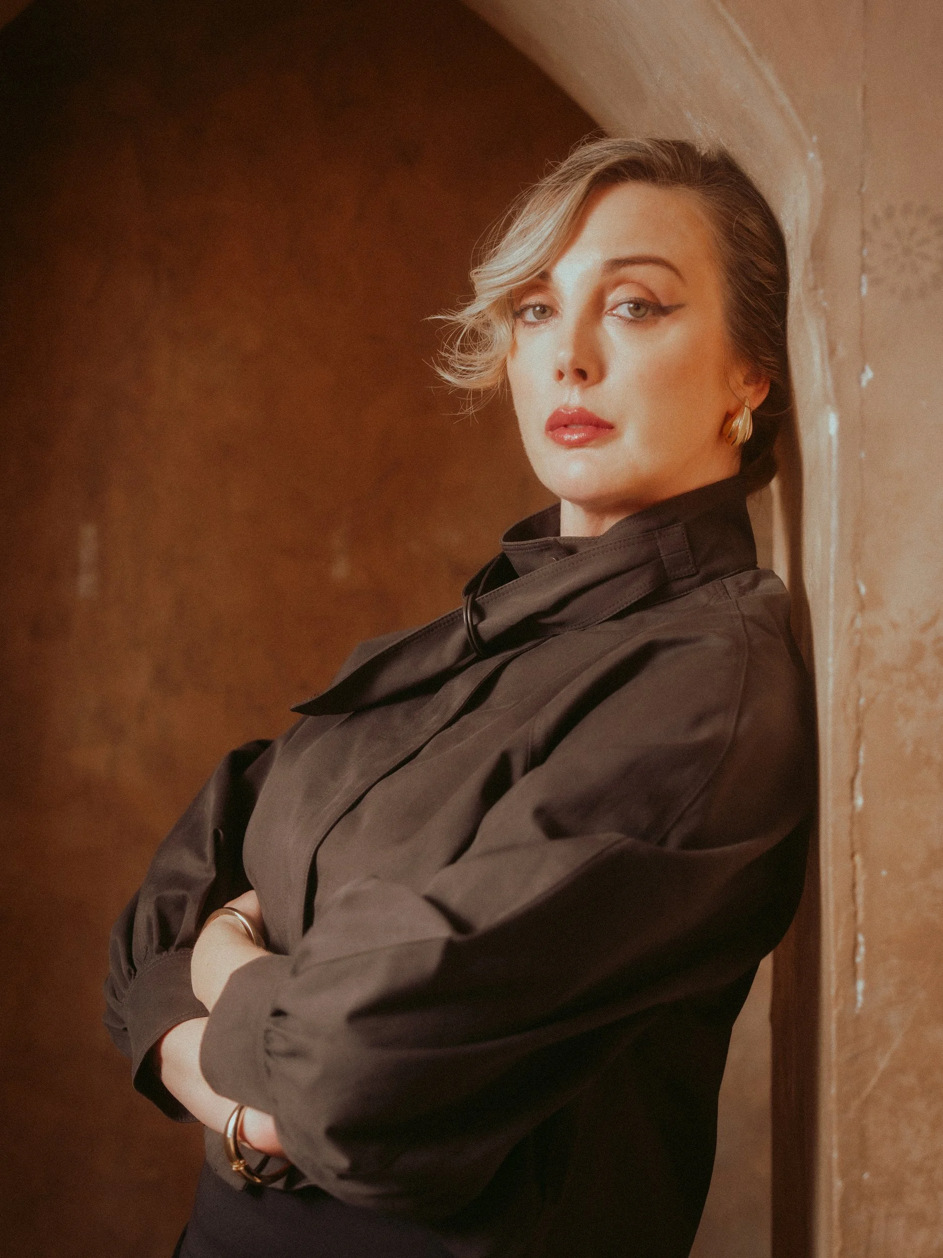 Milanka Brooks leaning in a clay arch in a black tie-neck jacket, editorial fashion photography by Osy Ikhile, Los Angeles