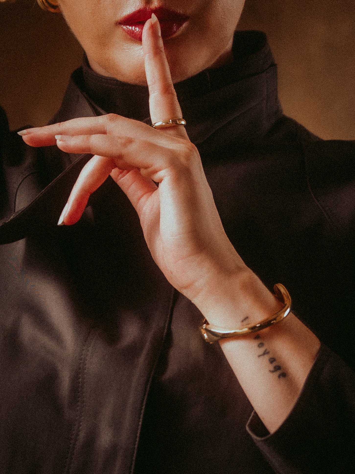 Close-up of Milanka Brooks with a finger to red lips, gold cuff and wrist tattoo, editorial fashion photography by Osy Ikhile, Los Angeles