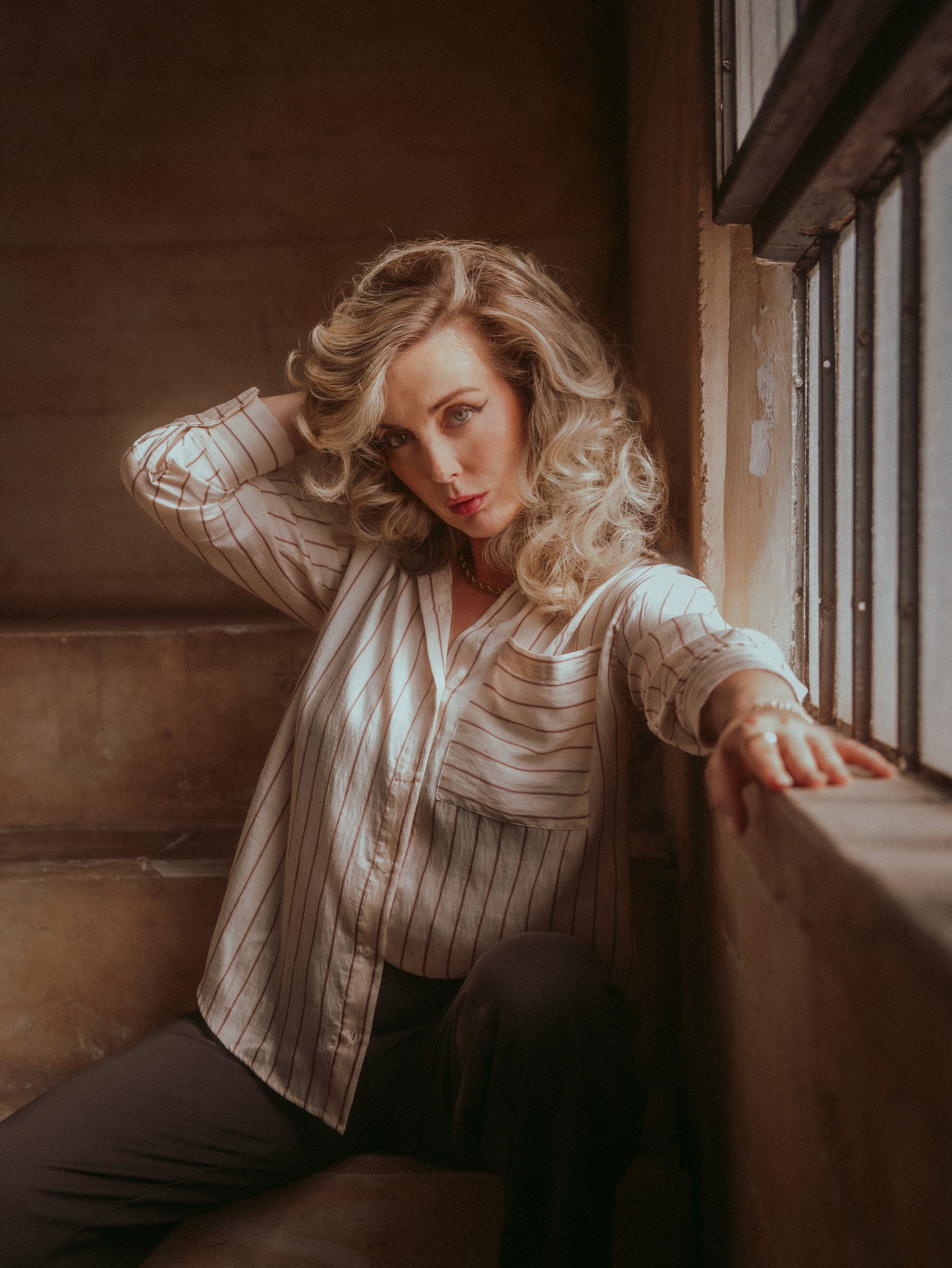 Milanka Brooks on a window ledge, hand in her hair, striped shirt, editorial fashion photography by Osy Ikhile, Los Angeles