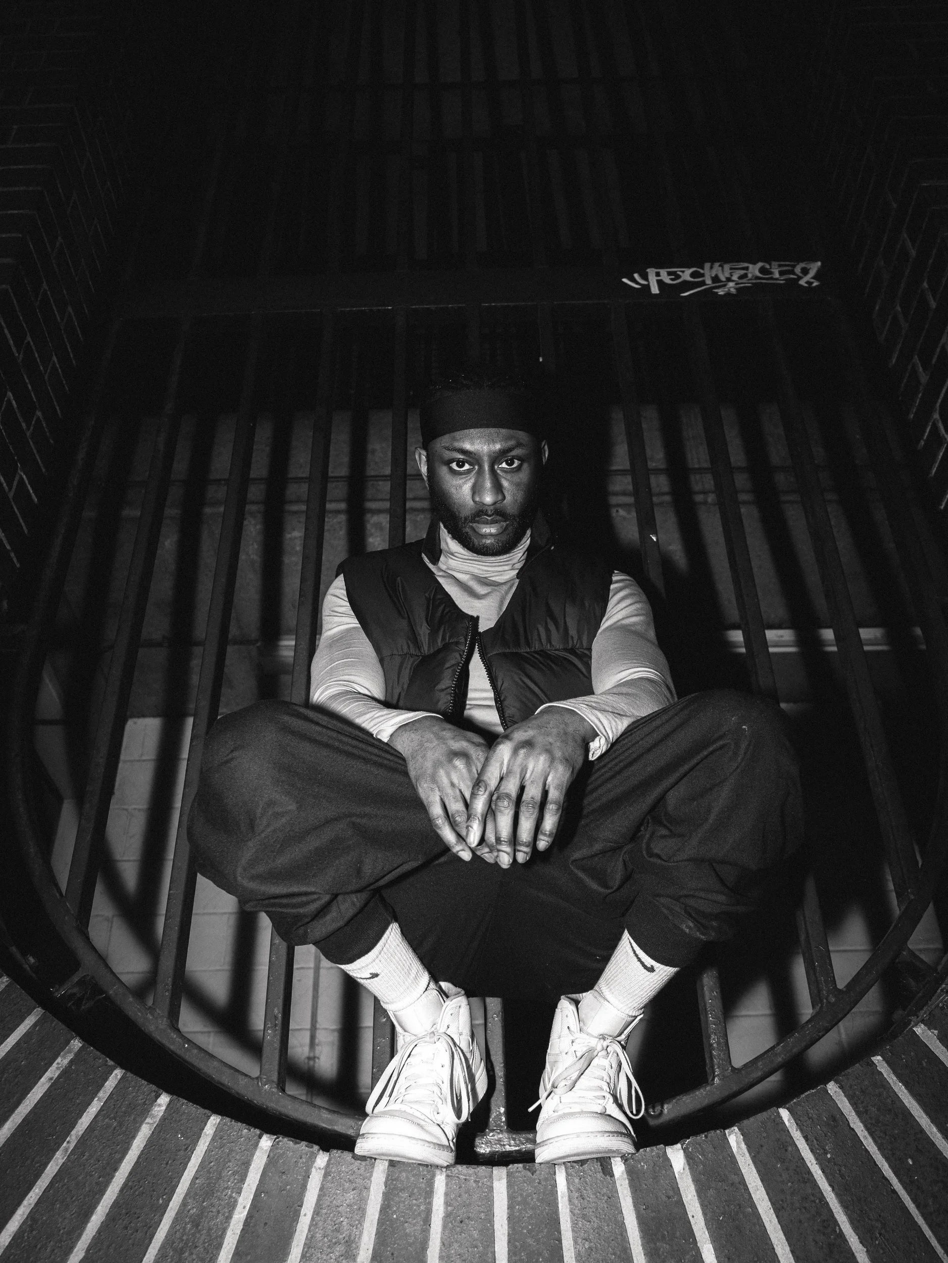 Paul Bossman sitting in a curved concrete space in a vest and white sneakers