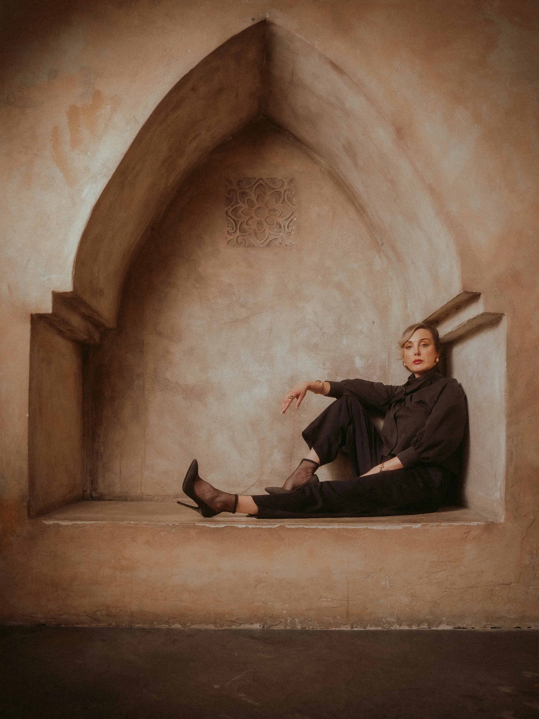 Milanka Brooks seated in a clay alcove in black tailoring, editorial fashion photography by Osy Ikhile, Los Angeles