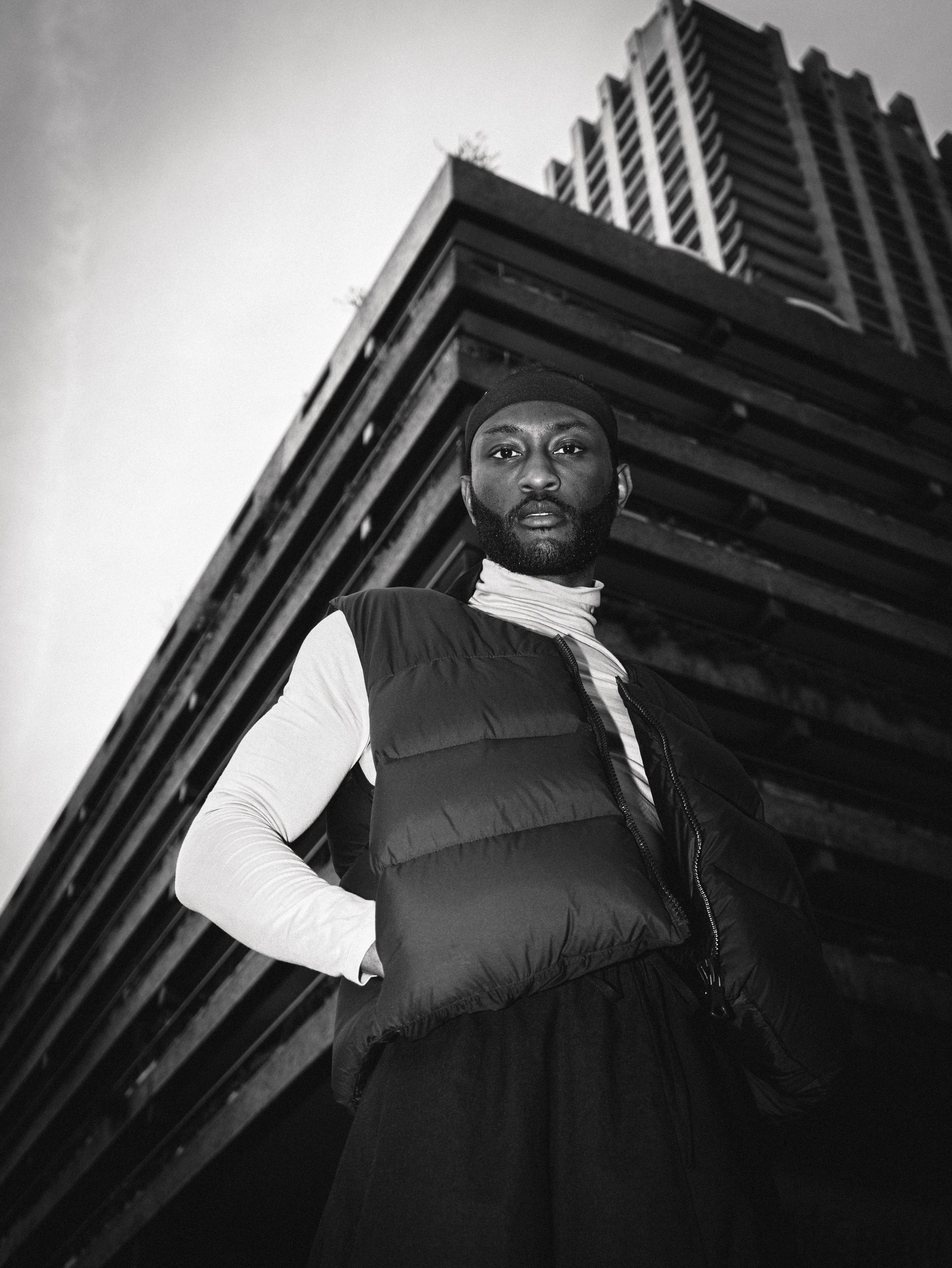 Paul Bossman in a puffer vest against brutalist architecture, black and white