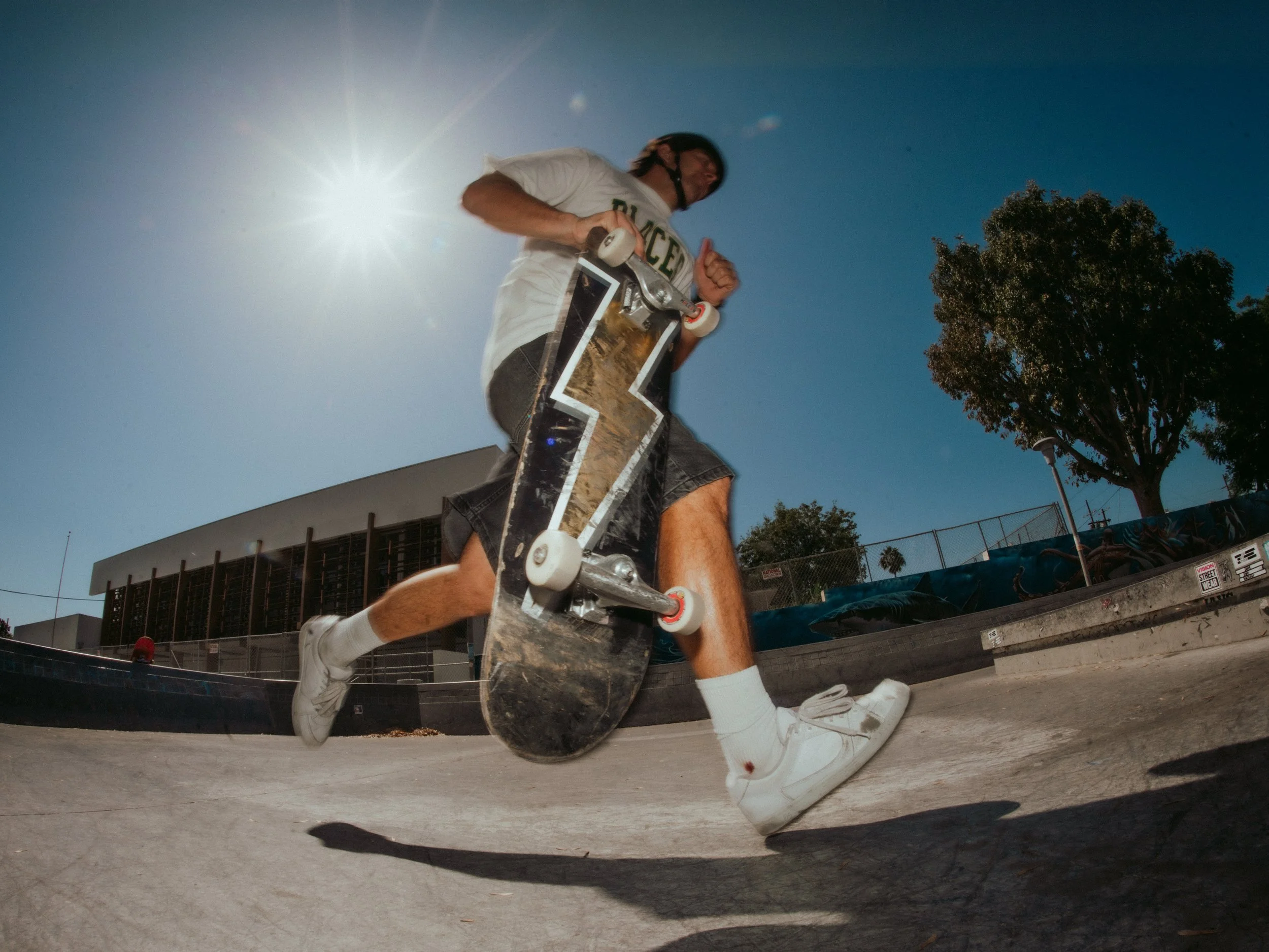 Brandon Loufas rolling in with his board, fisheye into the sun at the West LA Courthouse skatepark, Los Angeles skate photography by Osy Ikhile