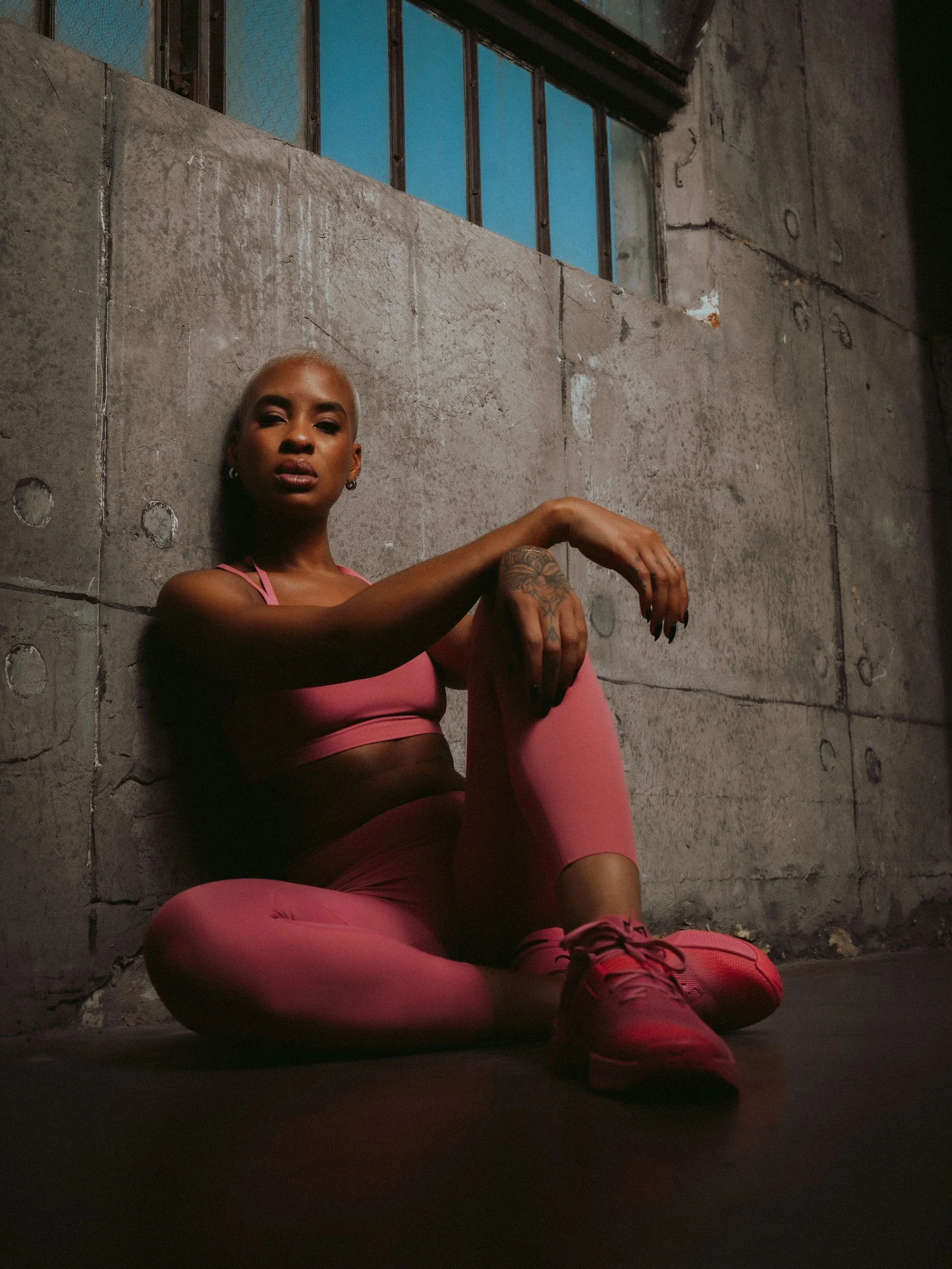 Athlete in a pink sports bra and leggings sitting against a concrete wall