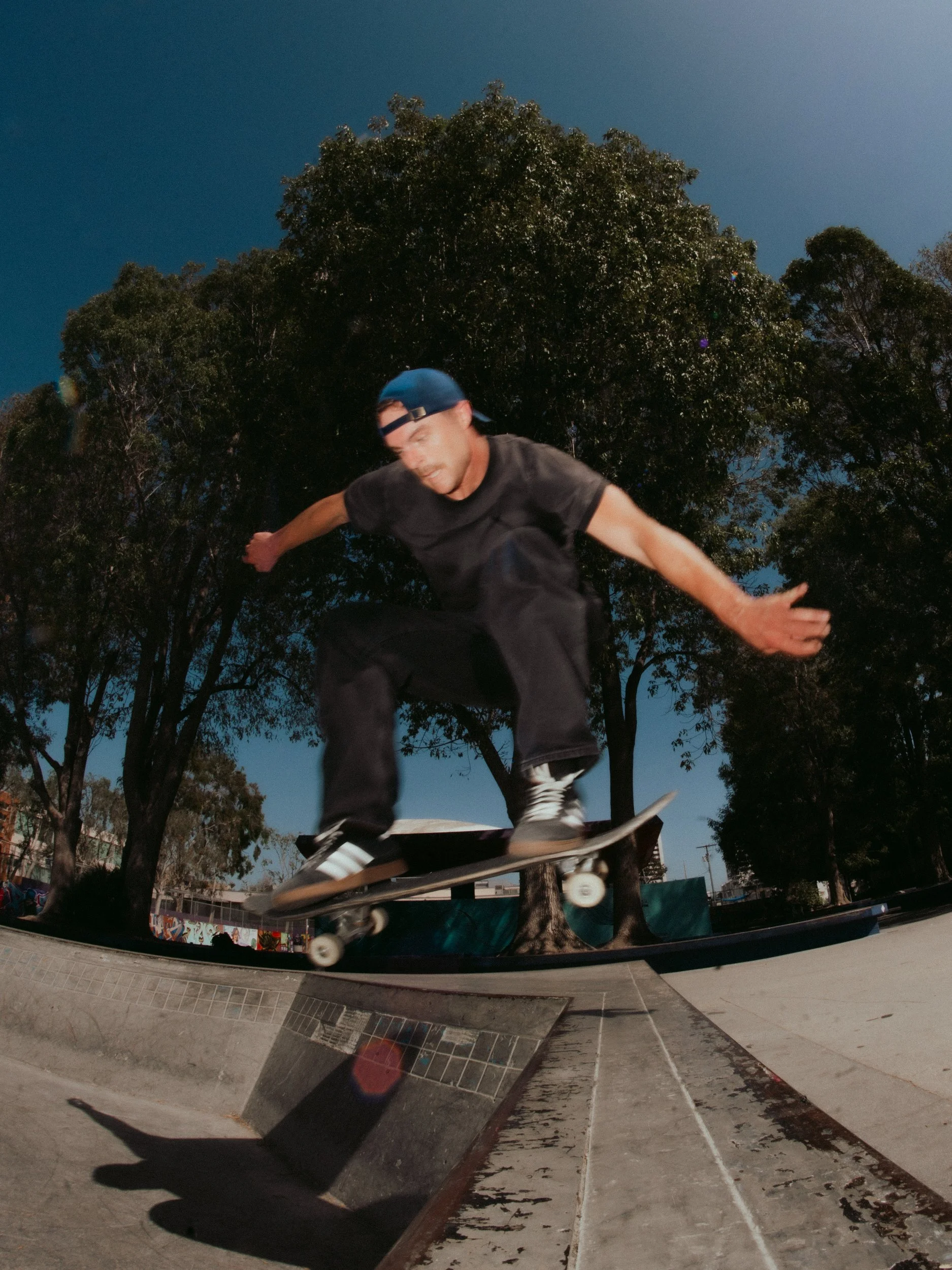 Isaiah Rojers mid-air, low angle fisheye at the West LA Courthouse skatepark, Los Angeles skate photography by Osy Ikhile