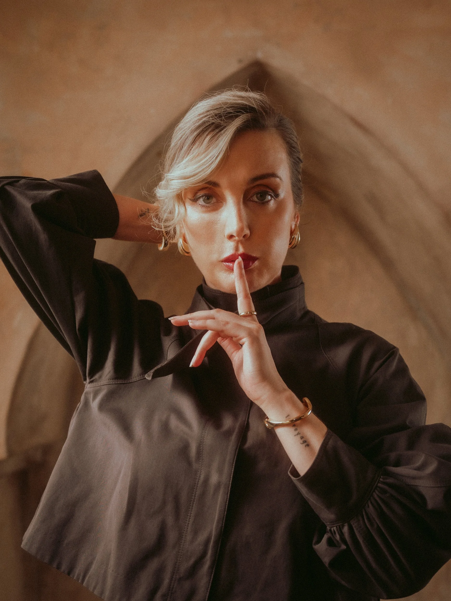 Milanka Brooks with a finger to her lips in a clay arch, editorial fashion photography by Osy Ikhile, Los Angeles
