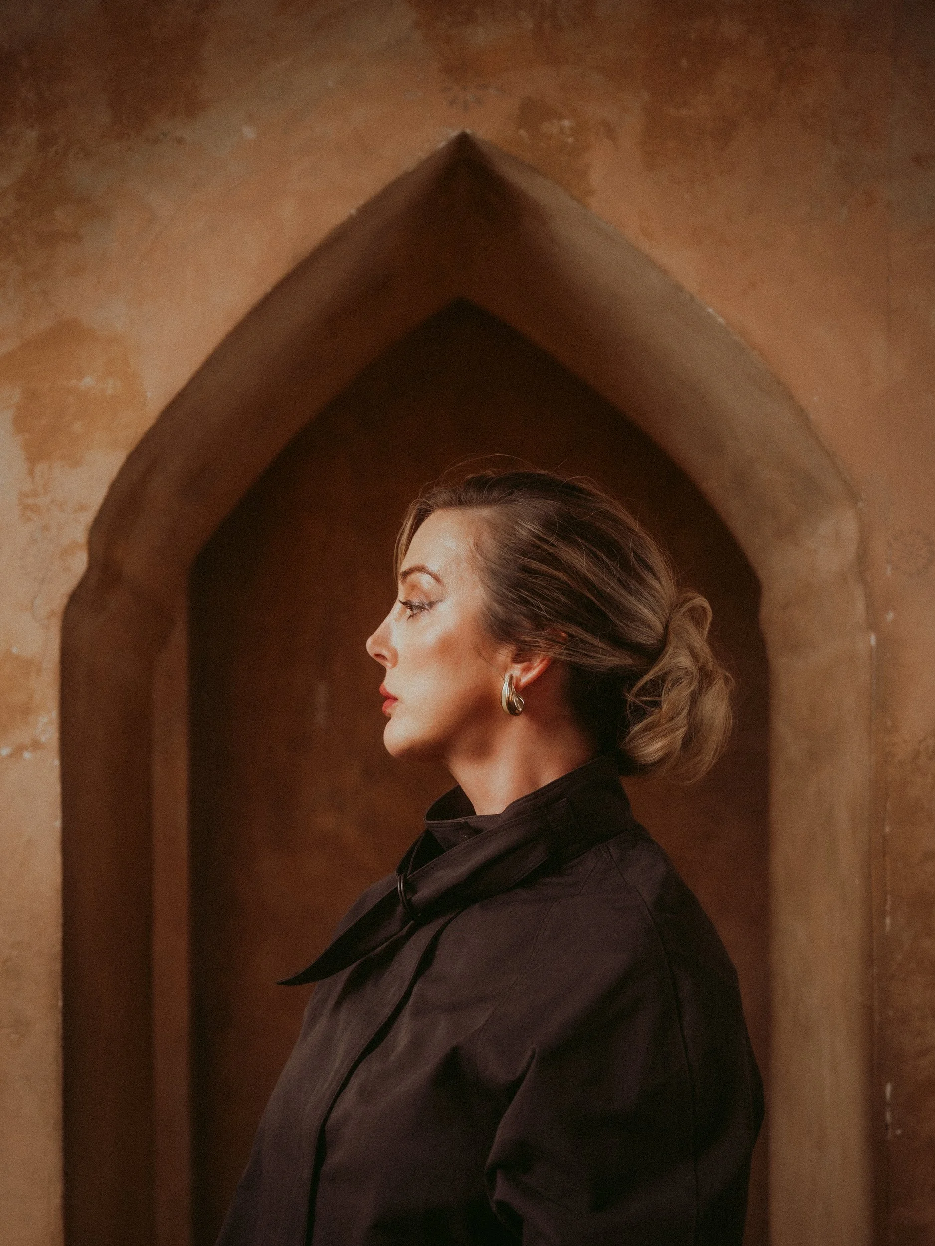 Milanka Brooks in profile inside a clay keyhole arch, black tailoring, editorial fashion photography by Osy Ikhile, Los Angeles