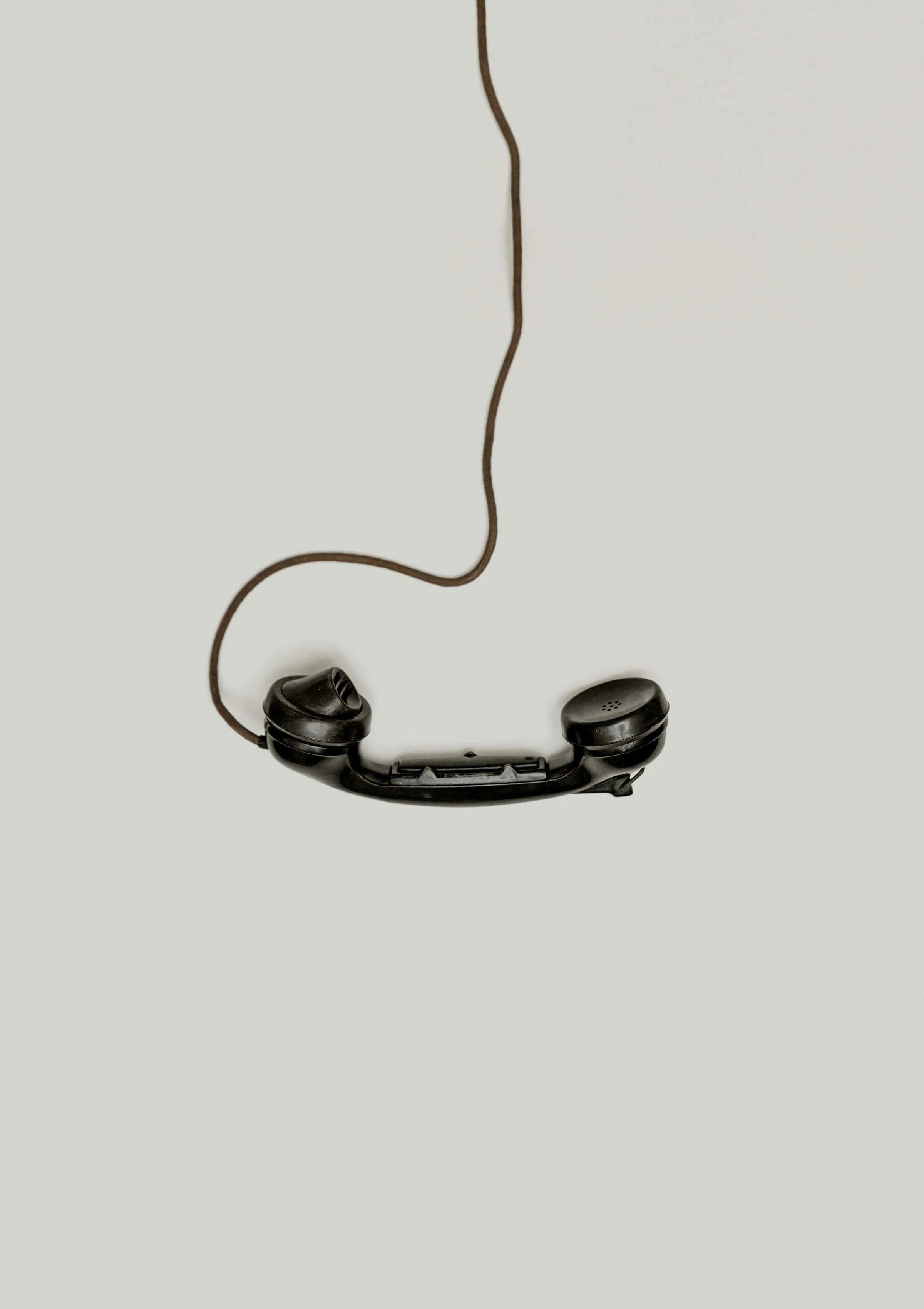 Wireless earbuds with a tangle of brown cord and black earbuds on a light gray background.
