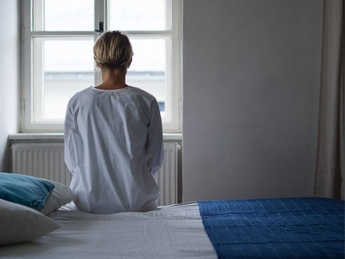 Person sitting alone on a hospital bed looking out a window, representing a mental health crisis and emergency treatment for bipolar disorder.