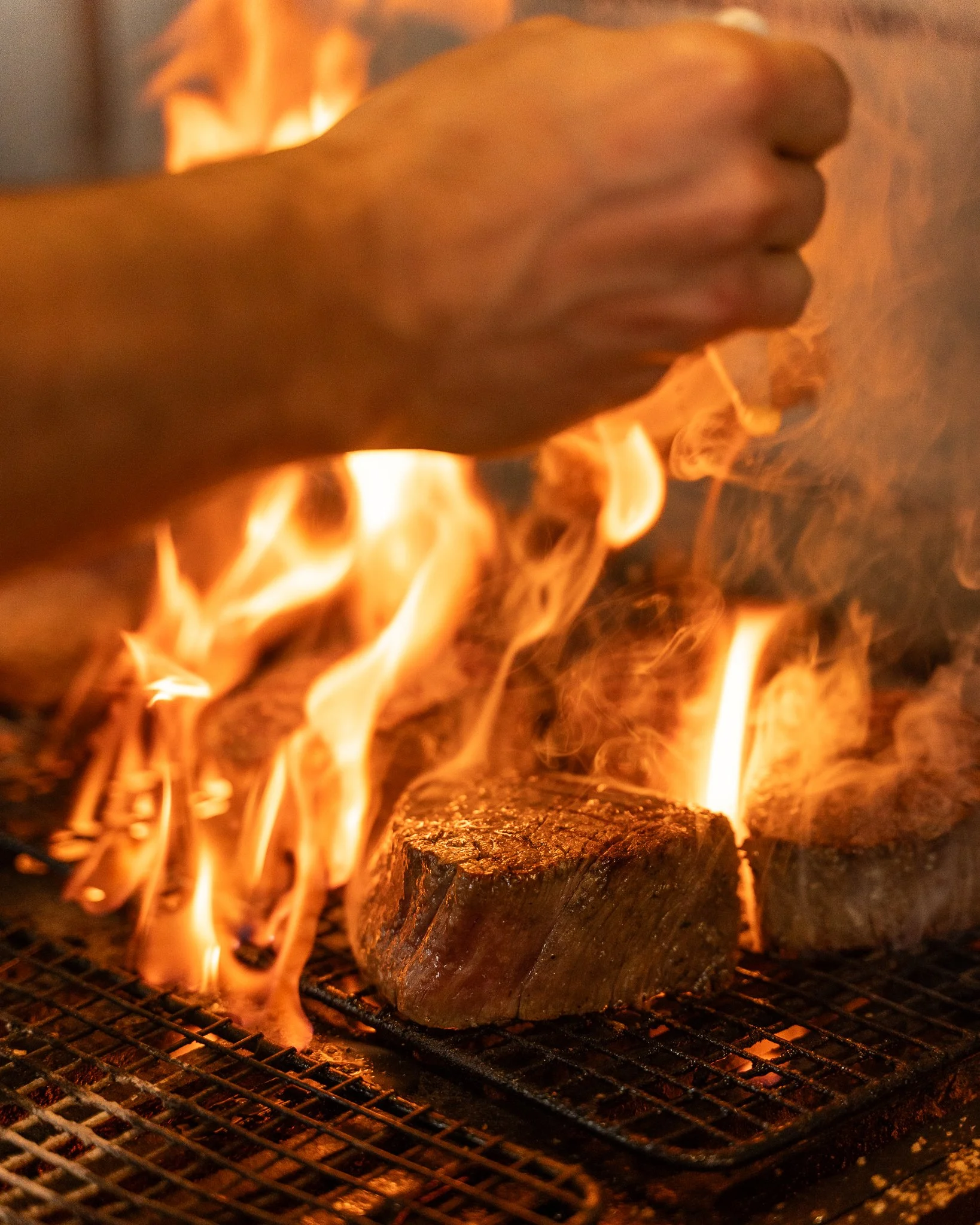 A close-up of a wooden log on a grill over open flames, with fire and blackened wood visible.