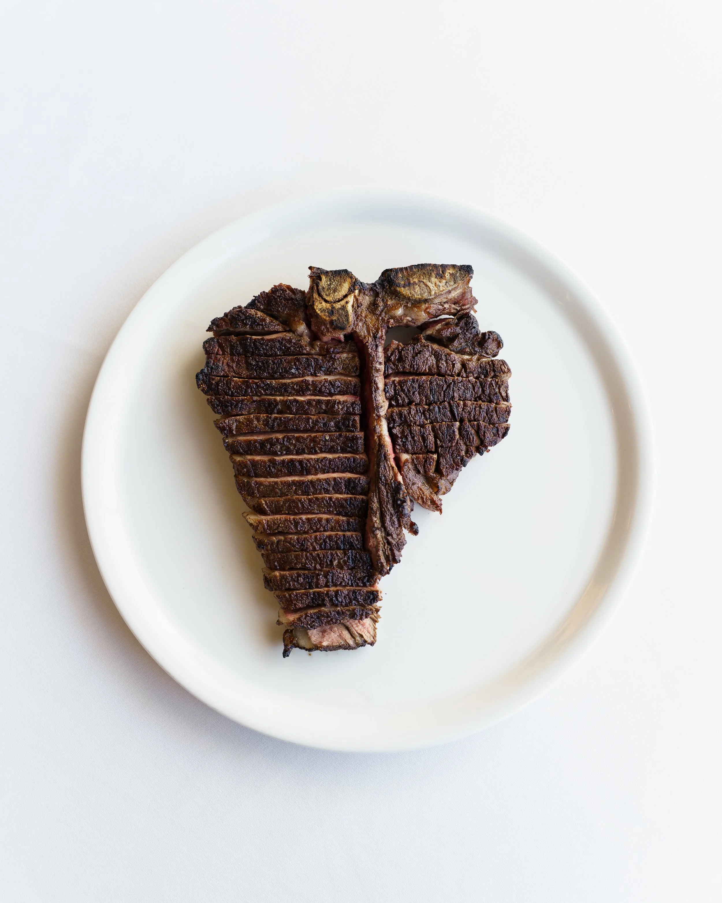 A white plate with a cooked beef short rib meat on top, dark brown in color, with visible grill marks, against a plain white background.