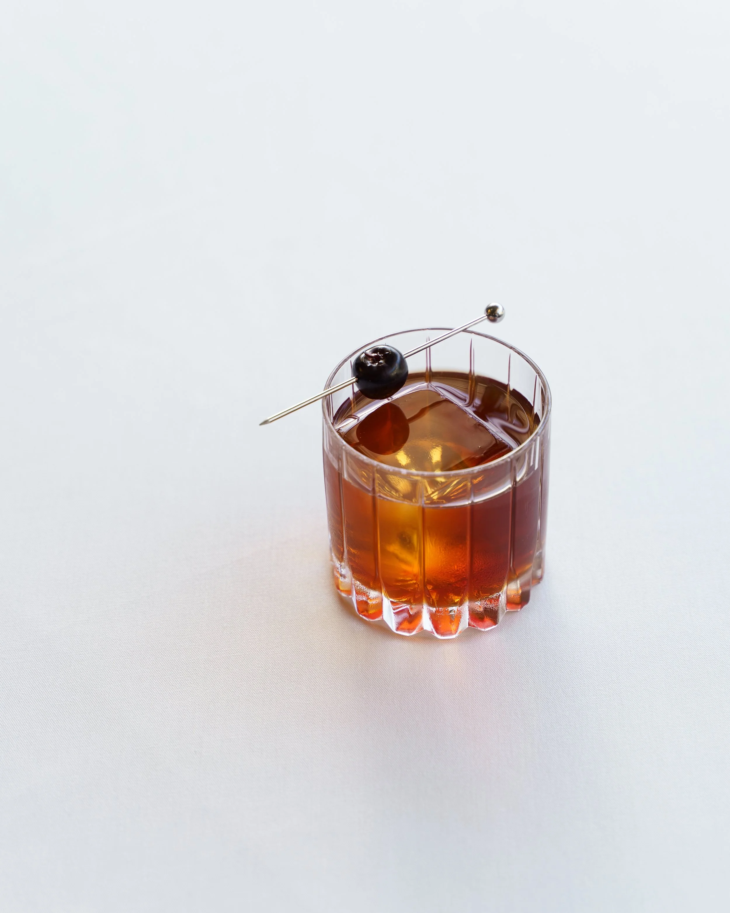 A cocktail with a black cherry resting on the rim.