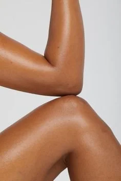 Close-up of a person's arm flexed with their fist raised and their thigh bent against a plain background.