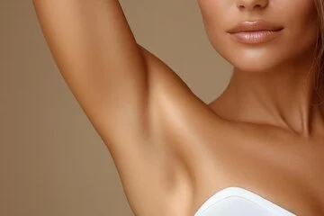 A woman with smooth skin showing her armpit, wearing a white strapless top against a beige background.