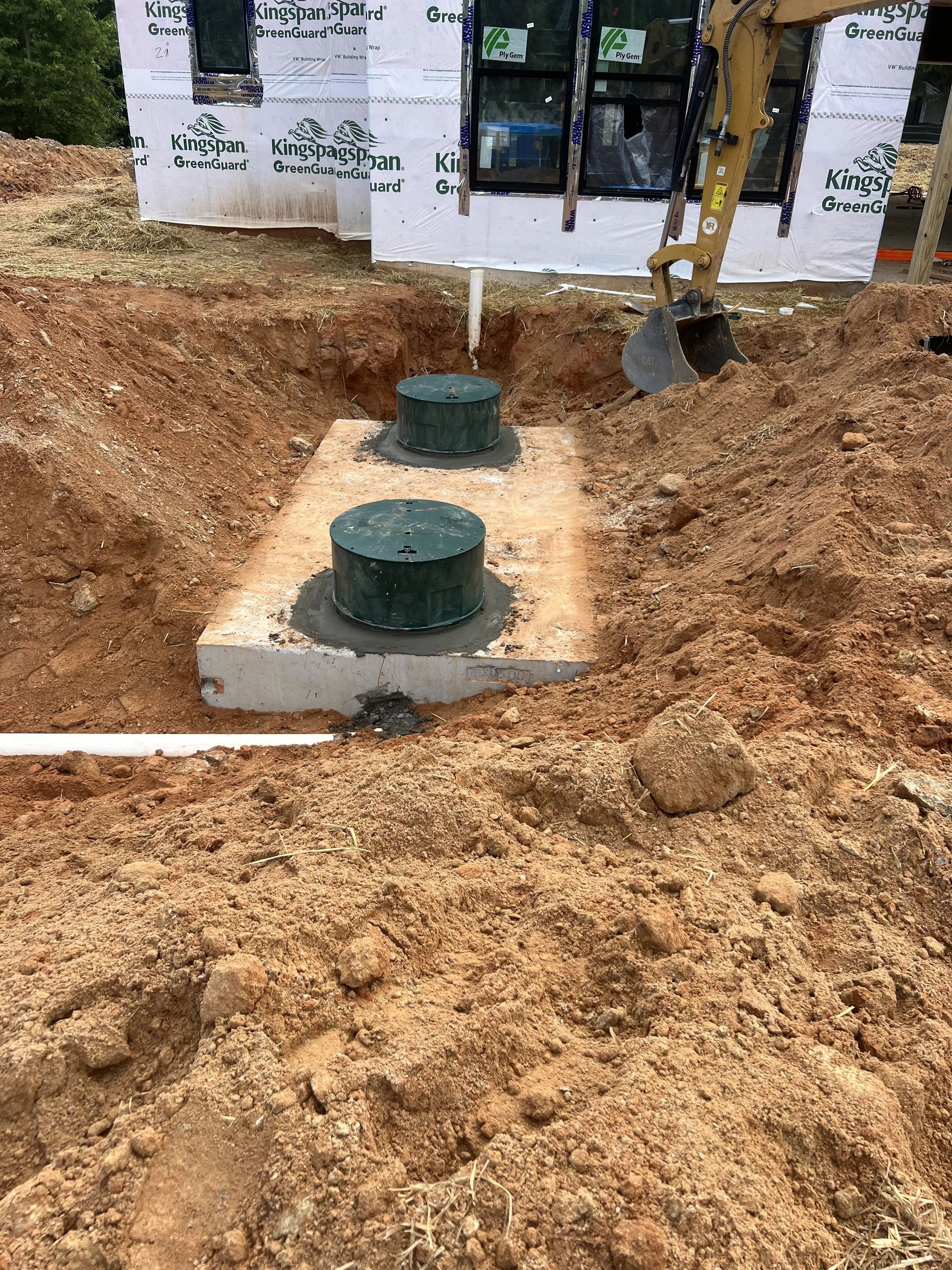 Underground utility access covers installed in a construction site with a house under construction in the background.
