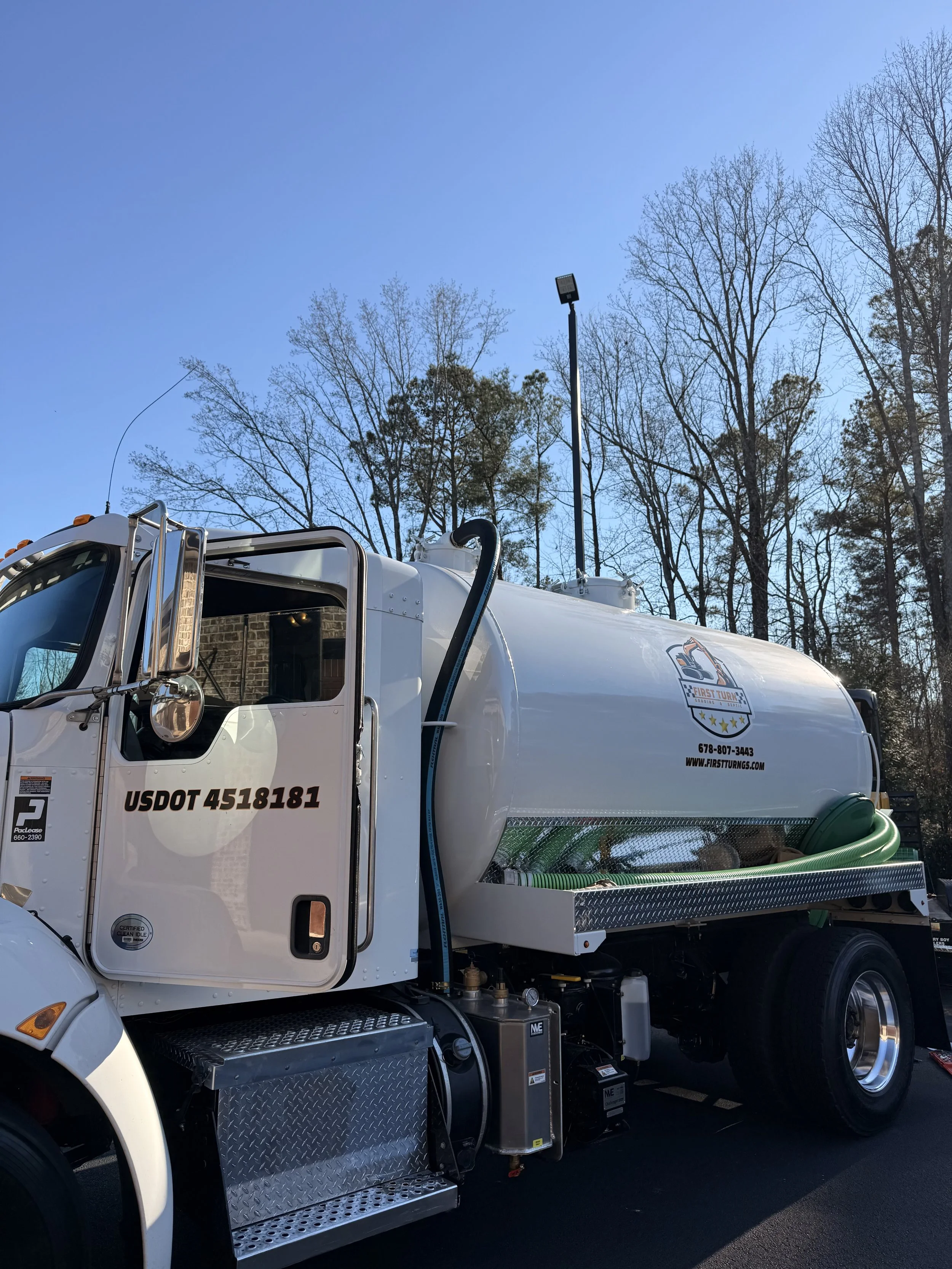 A white septic pump truck owned by First Turn Grading & Septic in a parking lot with blue skies