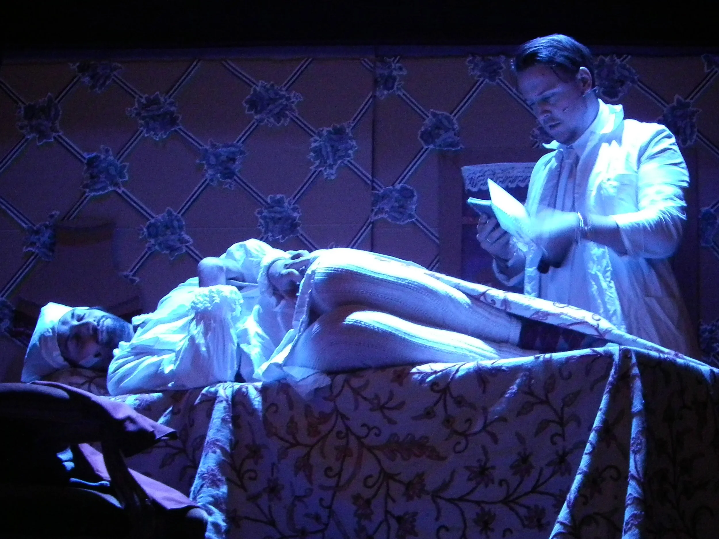 A scene depicting a person lying in bed, appearing unwell, with a doctor standing beside the bed, looking at a paper, illuminated by a blue light
