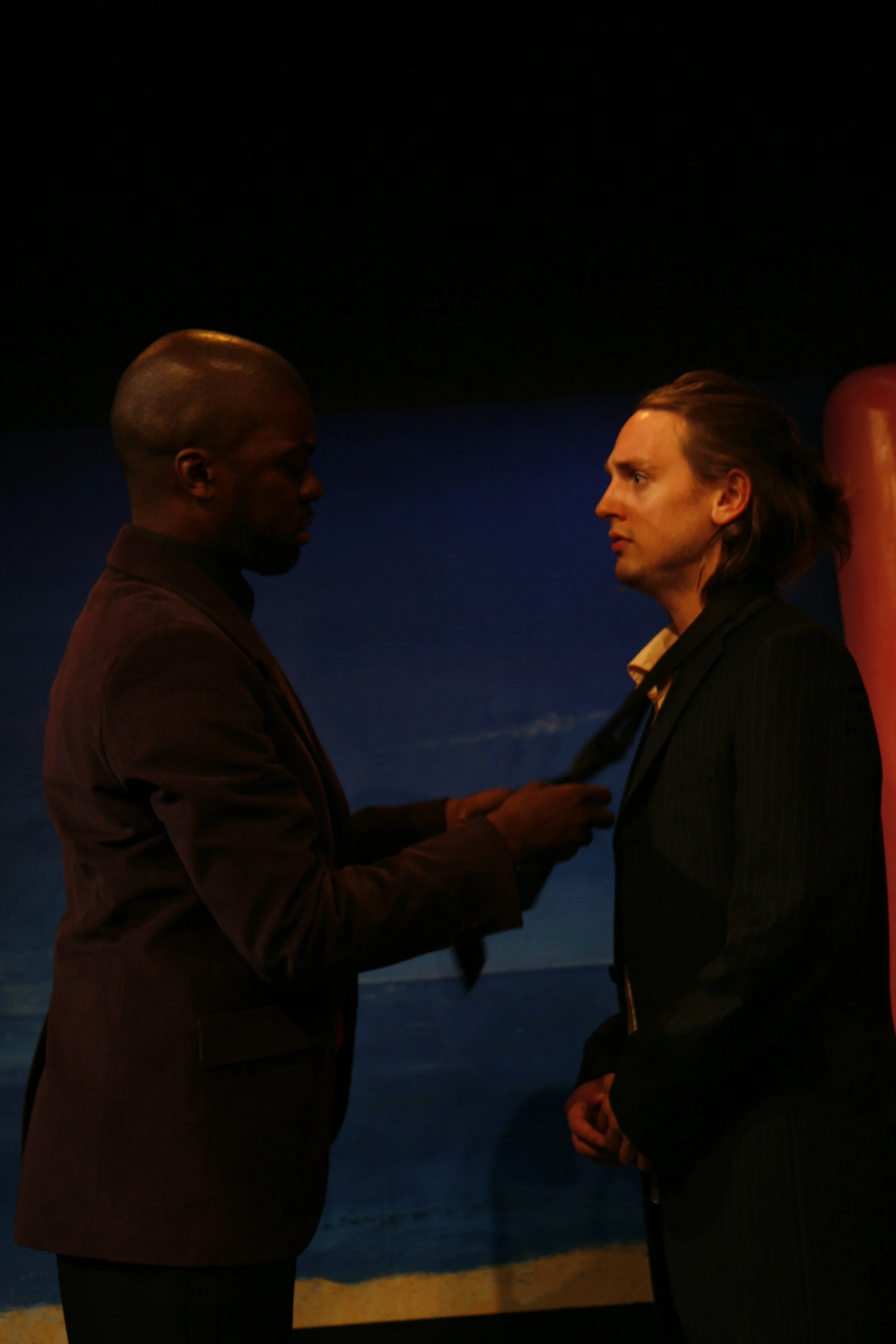 Two men in suits facing each other. One man is fixing the other's tie