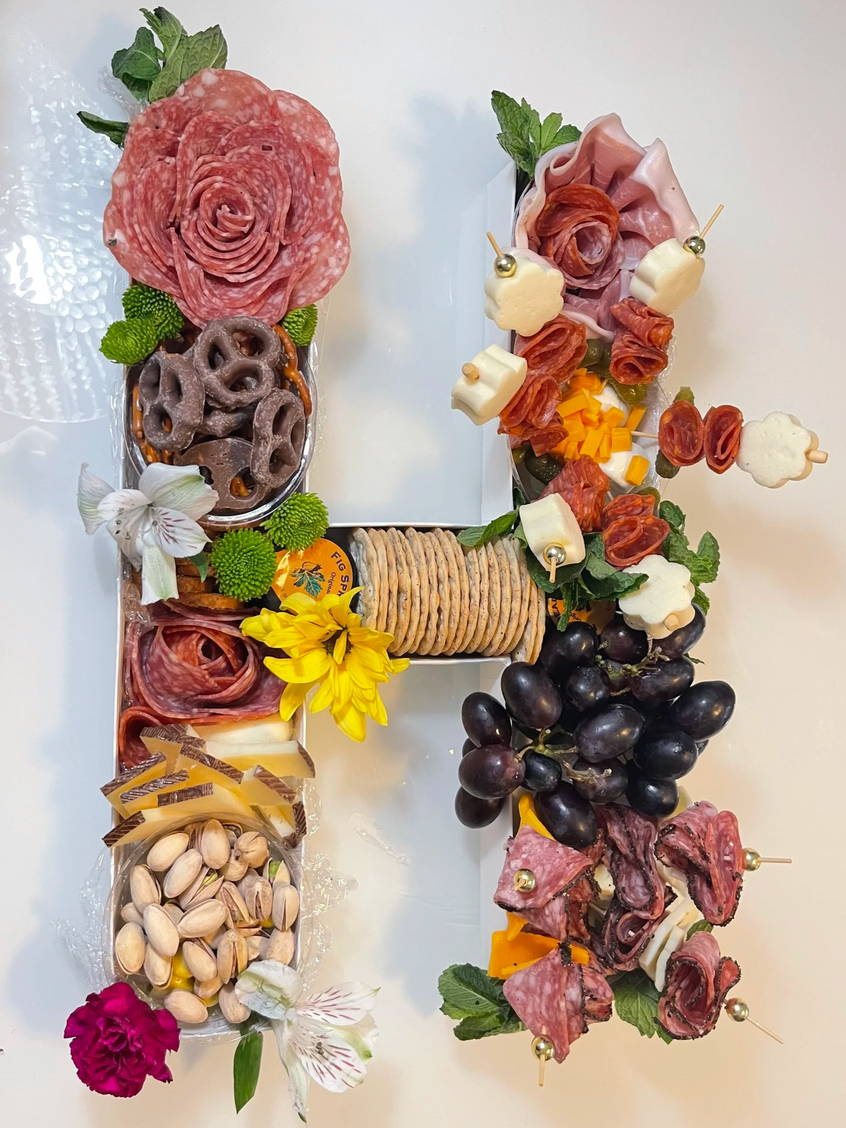 Forma de número 4 decorada con embutidos, quesos, frutas, galletas, nueces y flores.