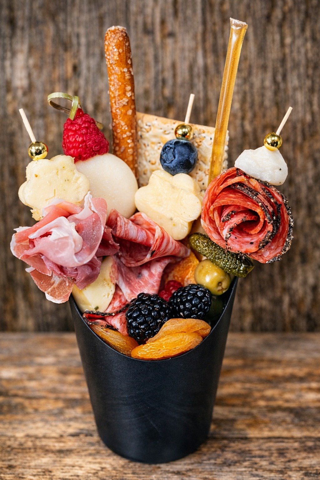 Copa con embutidos, quesos, frutas y galletas decorativas.