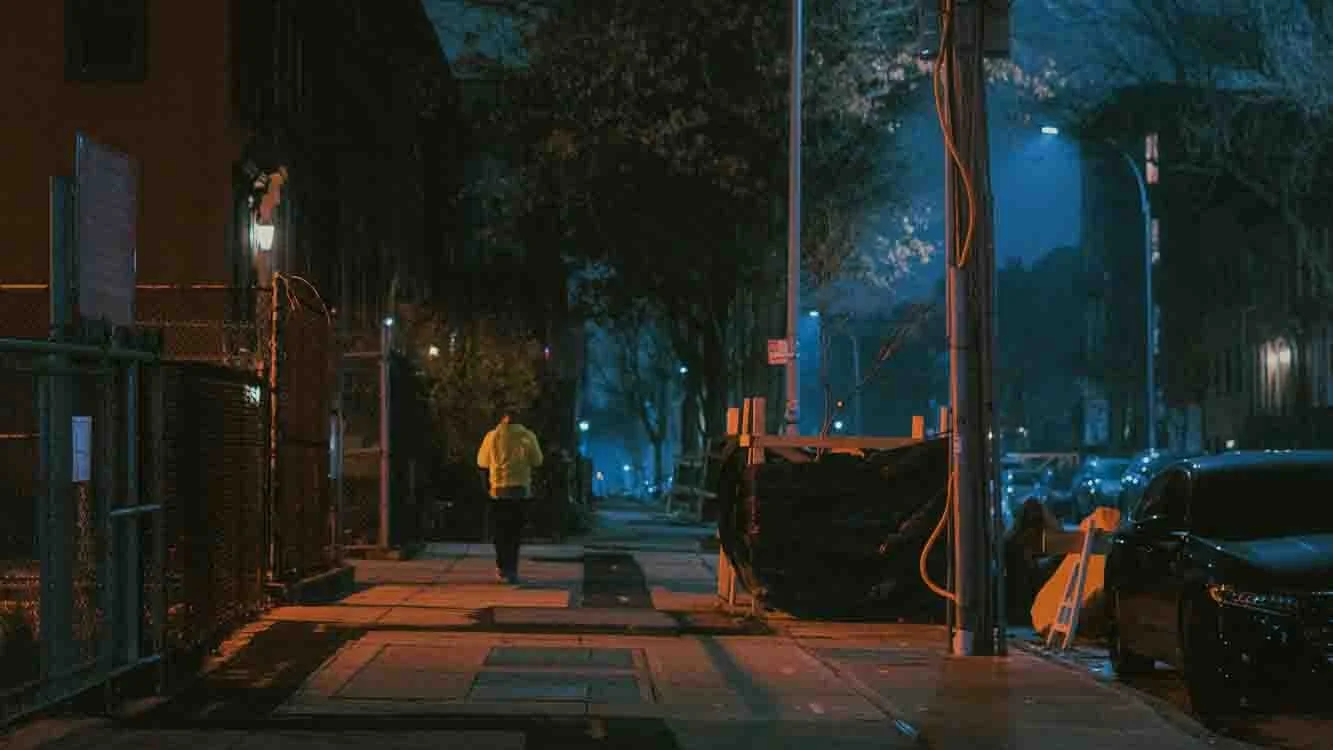 A person walking alone on a dimly lit city sidewalk at night.