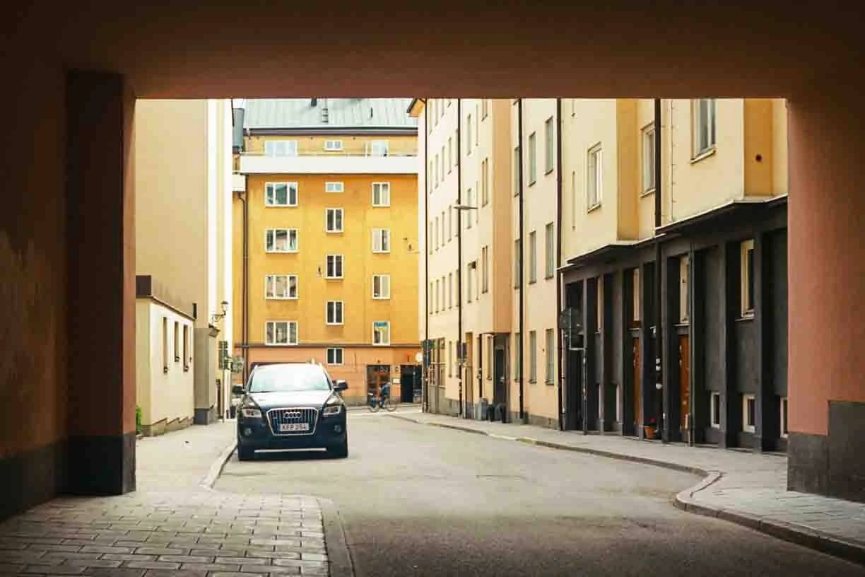 View of a narrow city street seen from under an archway, with parked cars and apartment buildings in the background.