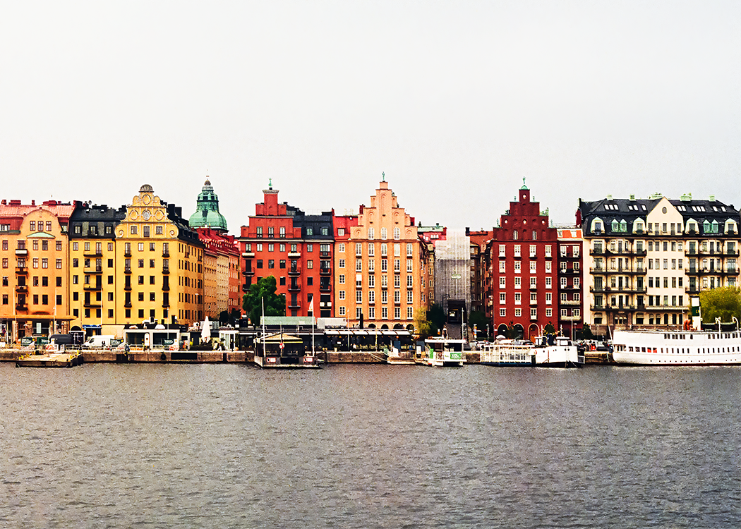 A row of colorful European style old buildings with boats in the river in front and a gray sky