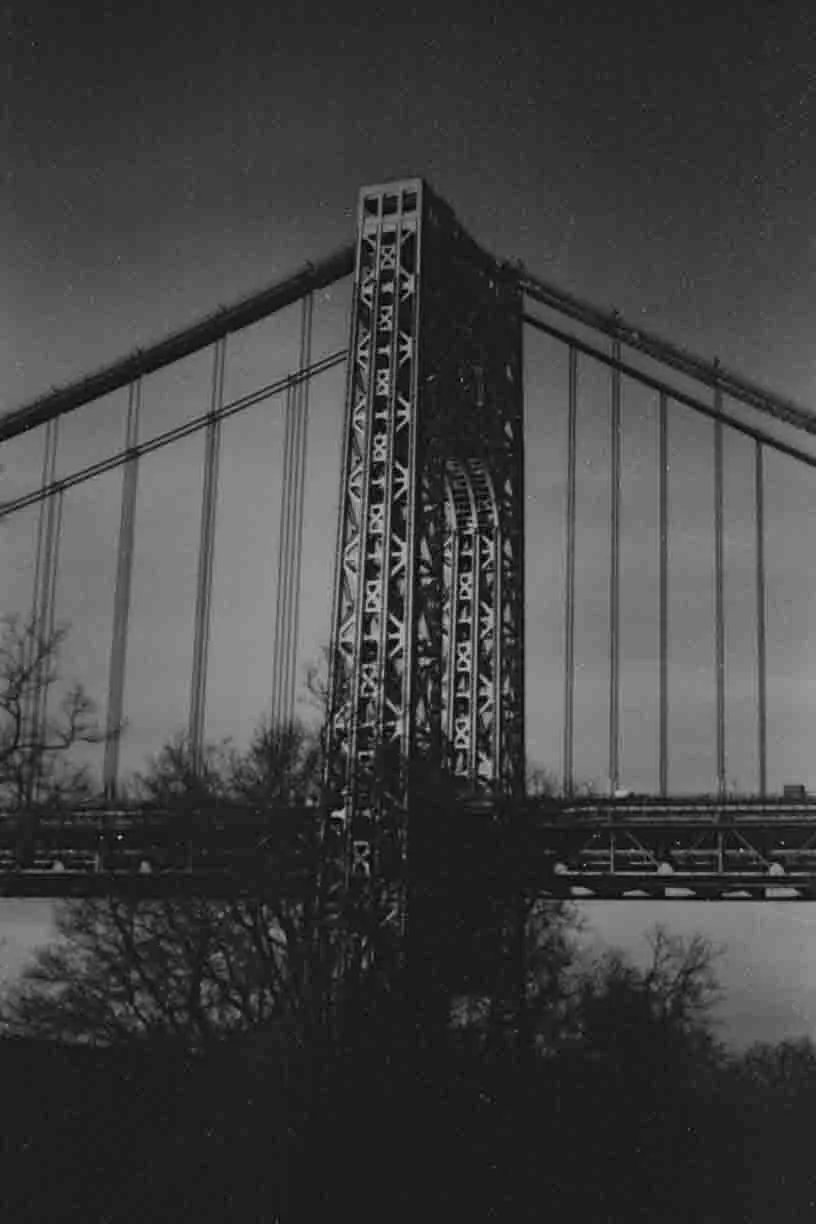Nighttime black and white photo of the Golden Gate Bridge's tower and suspension cables.