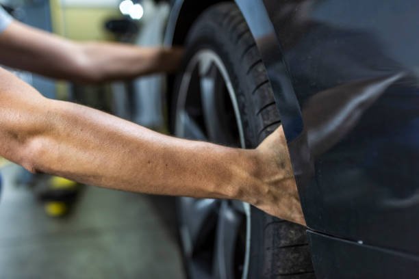A person's arm repairing or inspecting a black car tire in a garage or workshop.