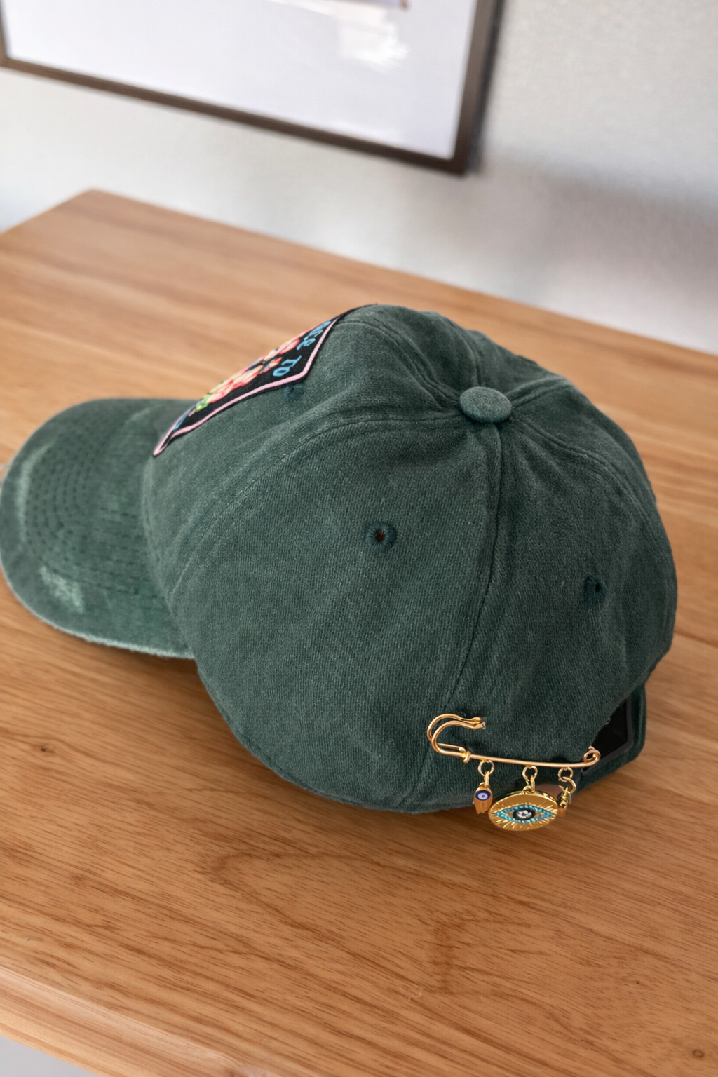 Green baseball cap with decorative pins resting on a wooden surface.