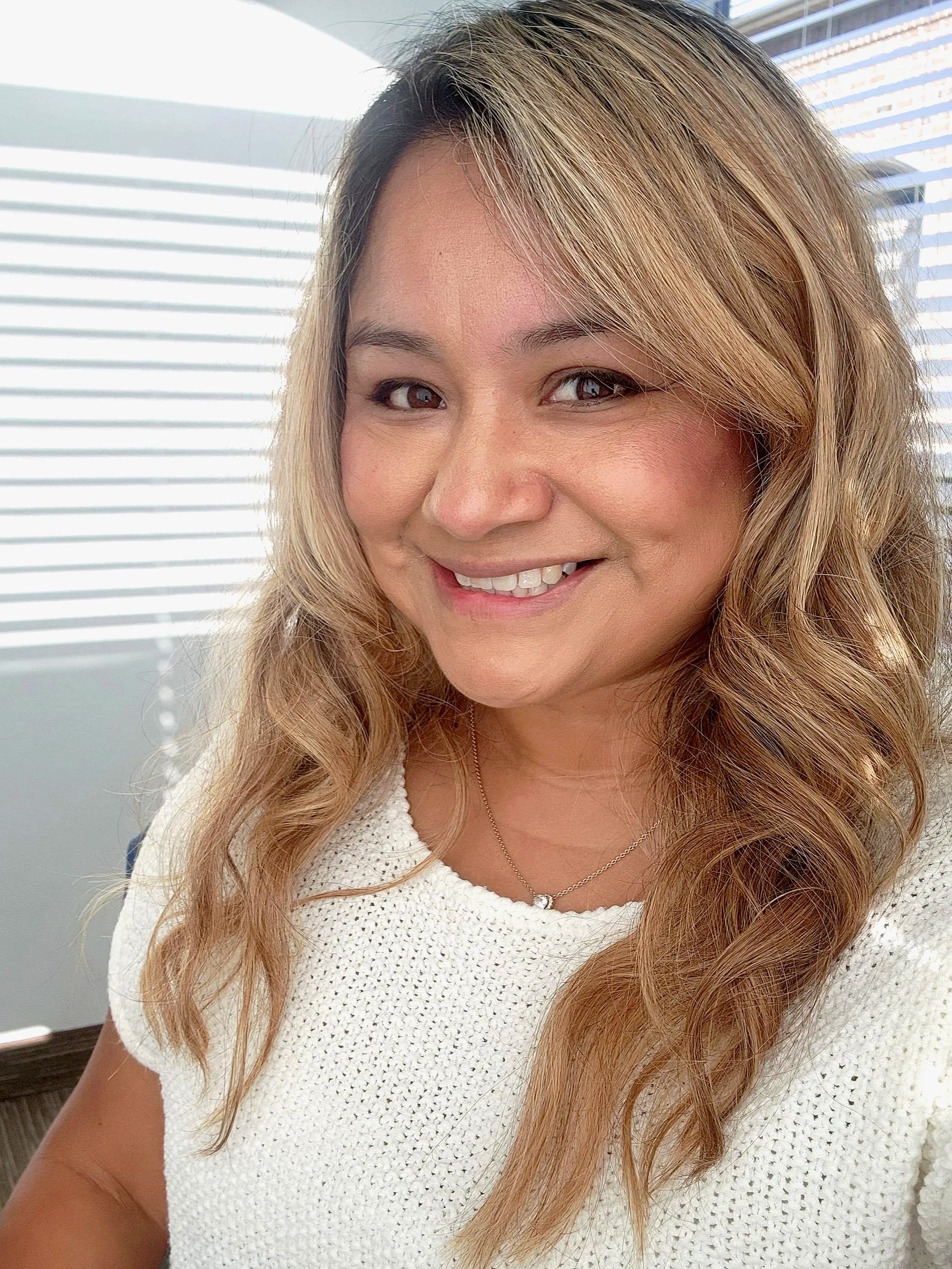 Retrato de una mujer sonriendo, con cabello largo y ondulado, usando una camiseta gris con logo de Nike.